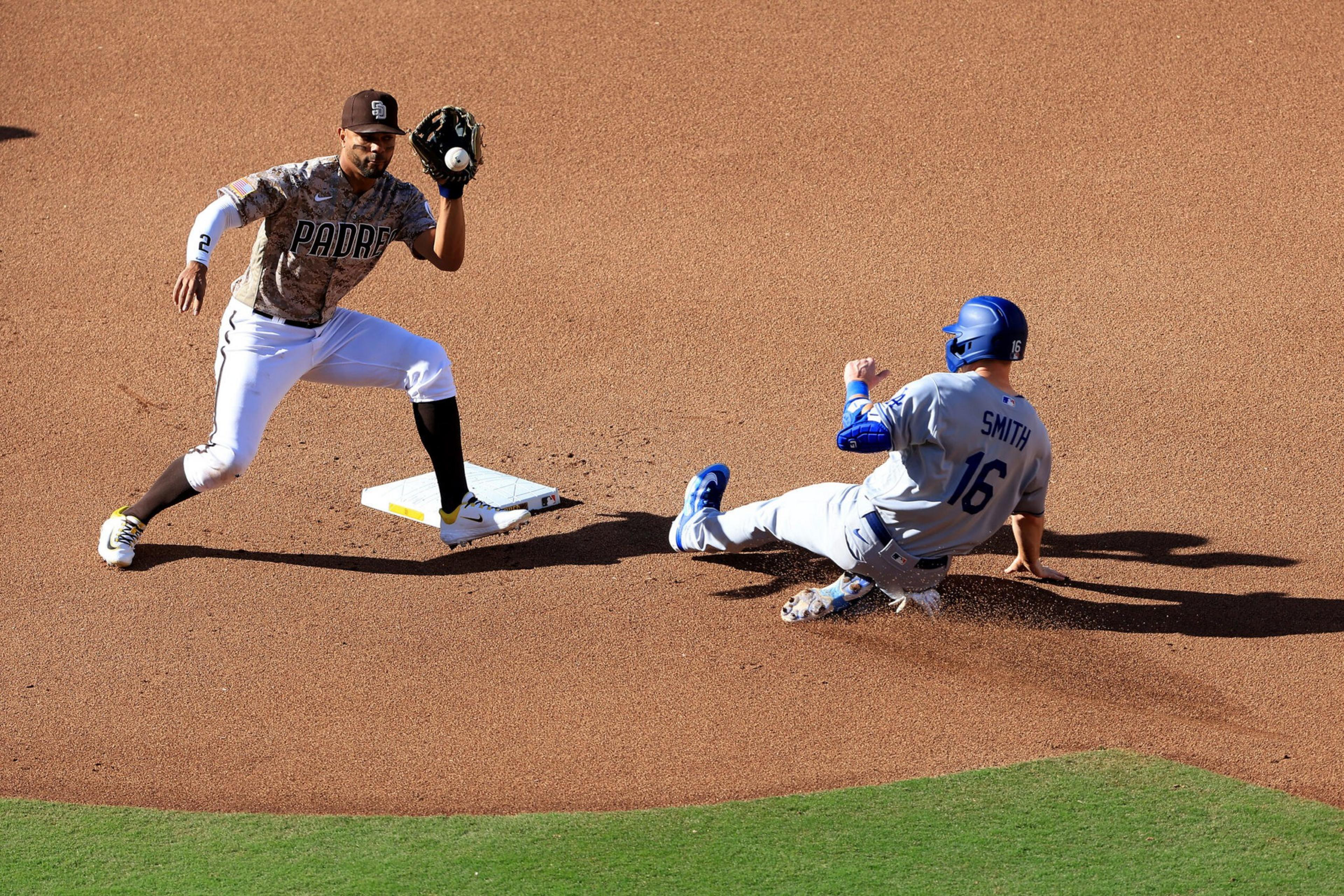A Padres player stands ready to catch a ball at second base as a player named Smith slides into the base, kicking up dirt.