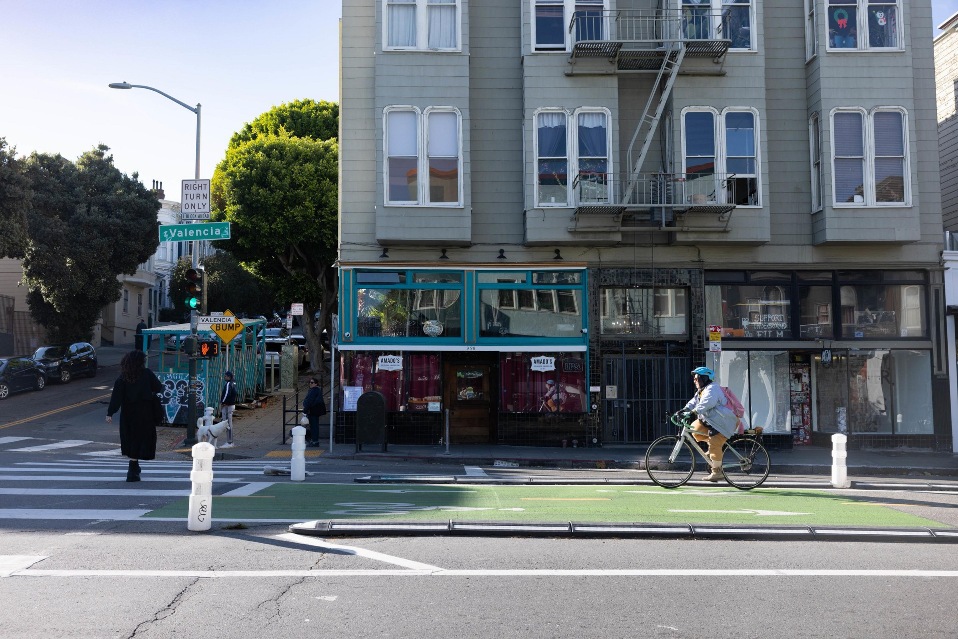 A cyclist and a person crossing the street in front of Amado's bar that is closing on Valencia St.  