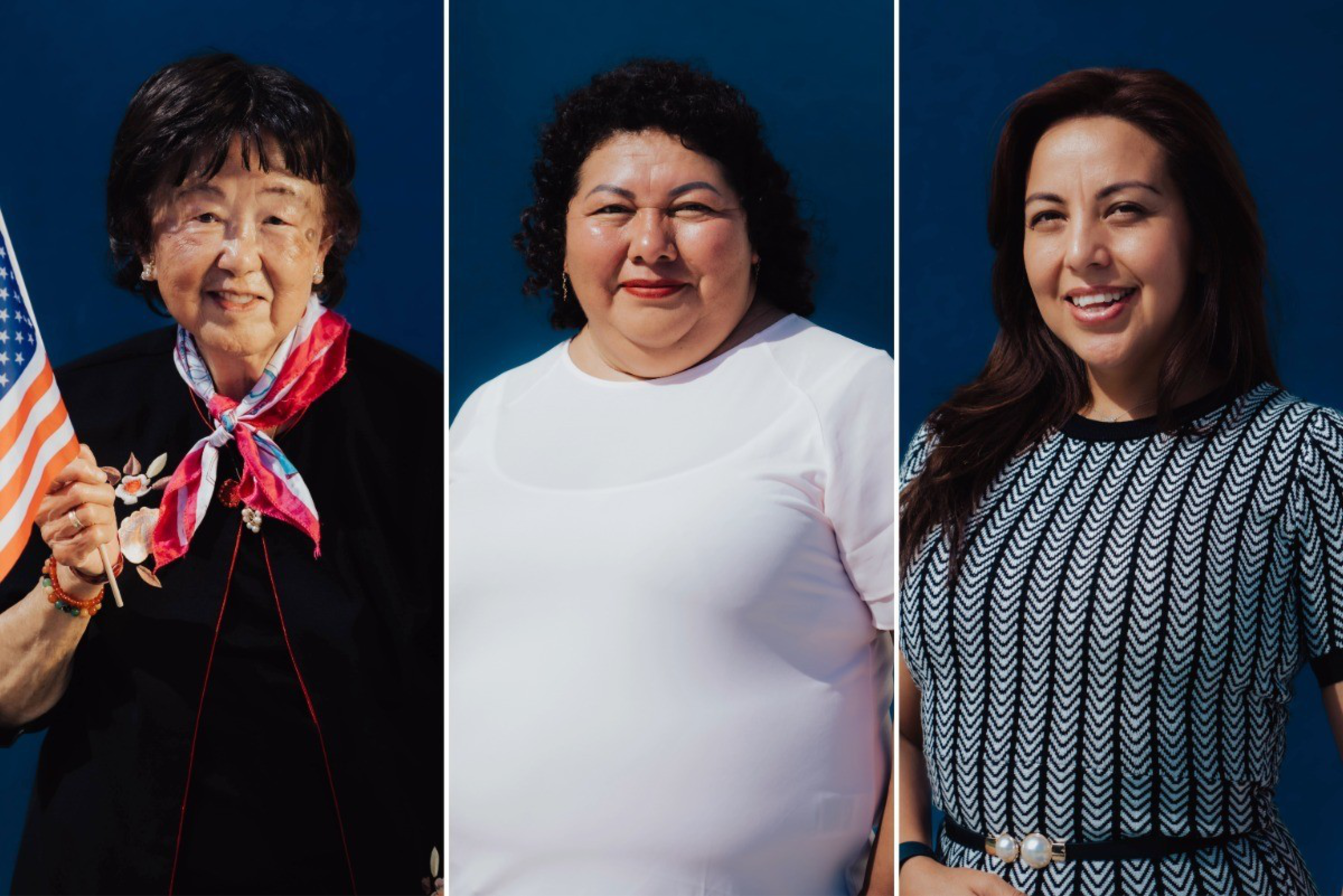 Three women stand against a dark blue backdrop; the first holds an American flag, the second wears a white top, and the third wears a black-and-white patterned dress.