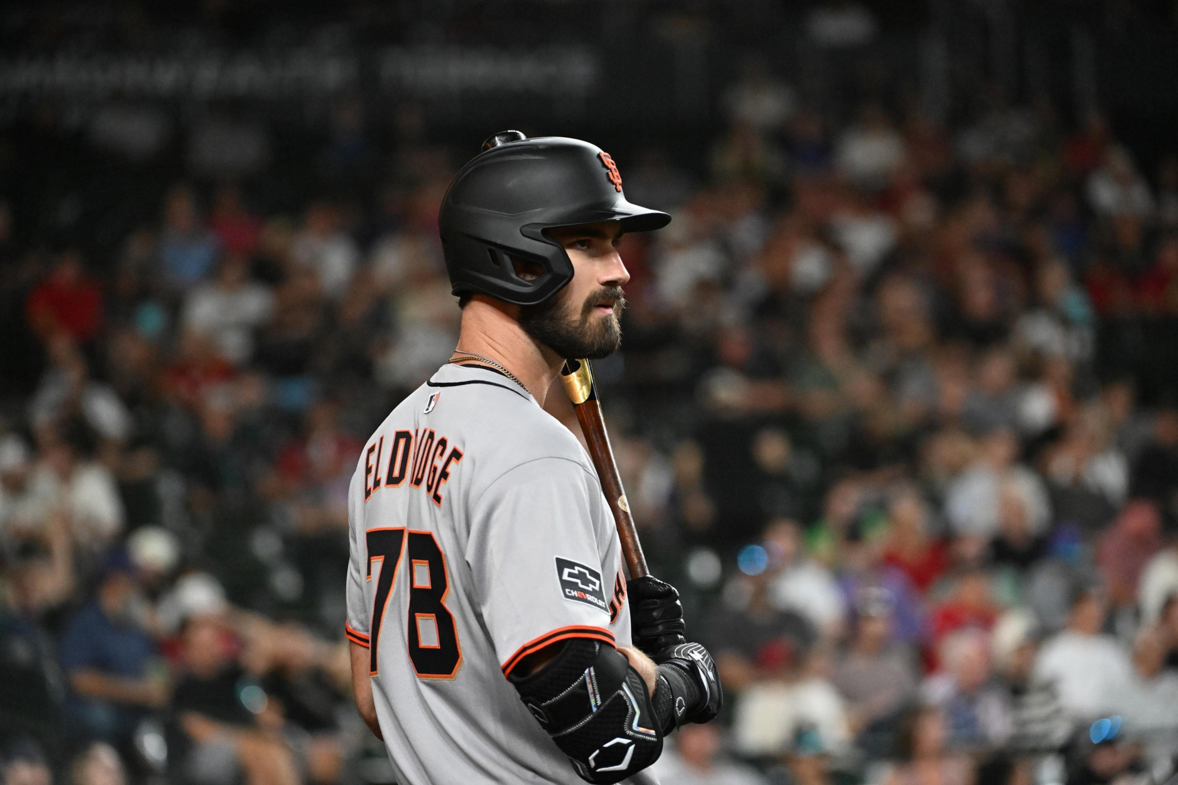 A baseball player wearing a gray jersey with "BELDIGE" and number 78 stands holding a bat, wearing a black batting helmet, with a blurred crowd behind him.