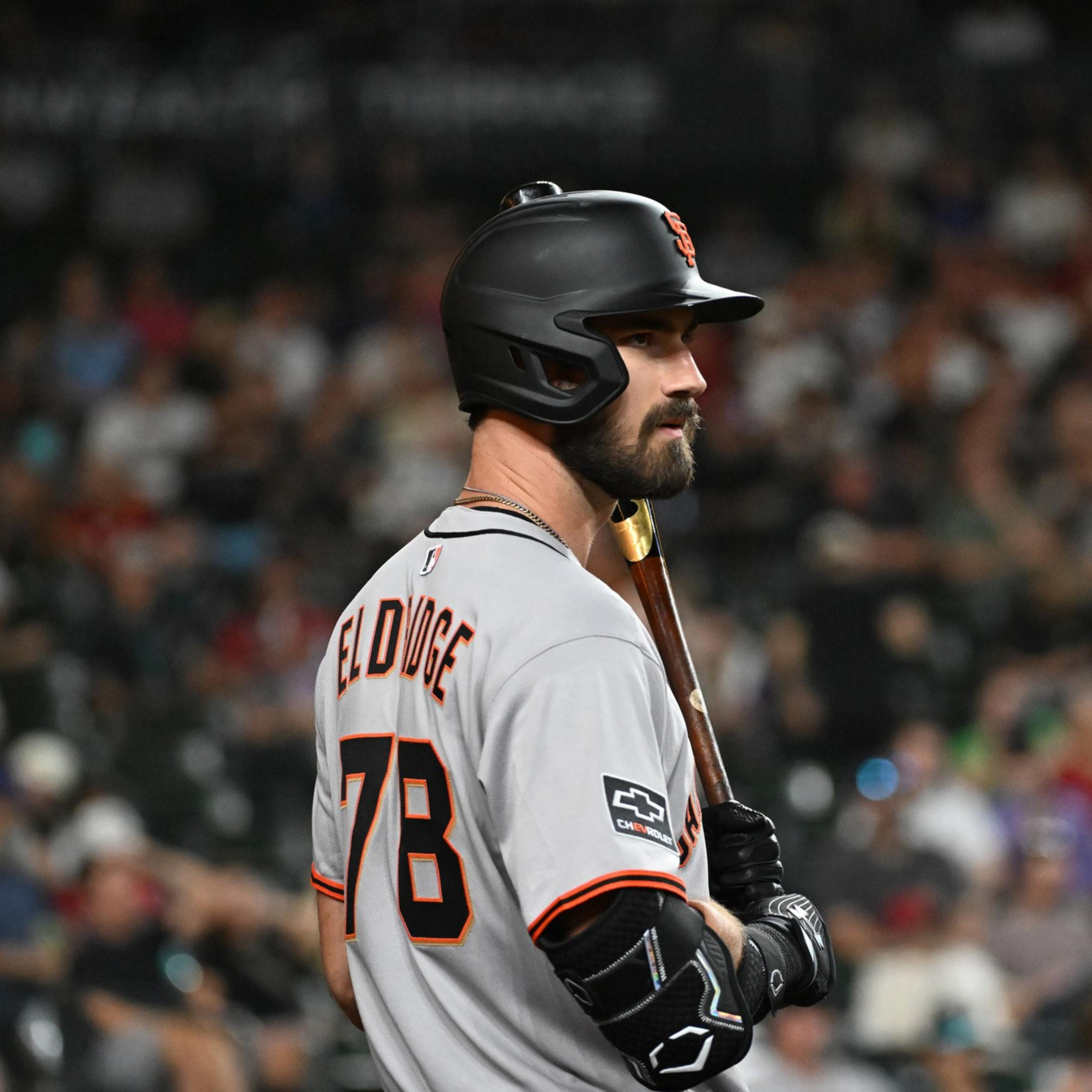 A baseball player wearing a gray jersey with "BELDIGE" and number 78 stands holding a bat, wearing a black batting helmet, with a blurred crowd behind him.