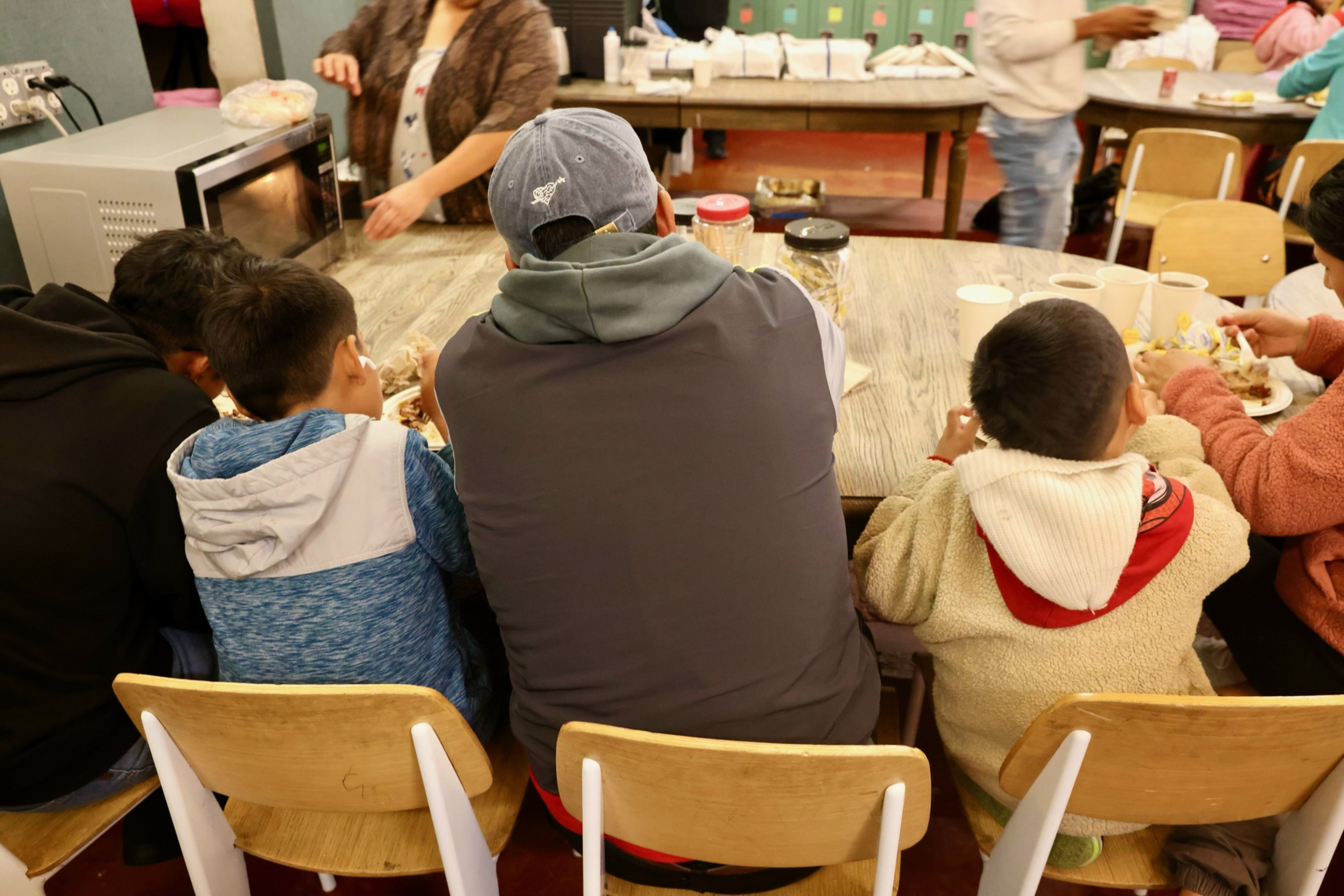 One adult and three kids sit at a table to eat in a dining hall.