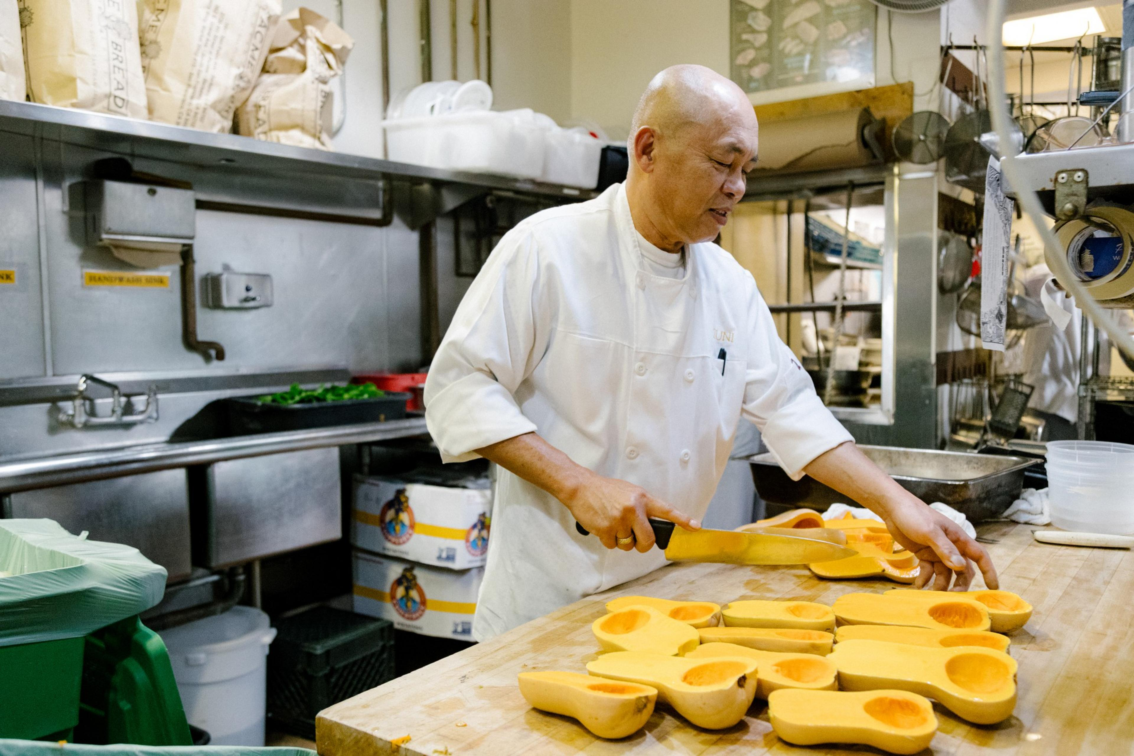 A chef cuts squash in a kitchen area.