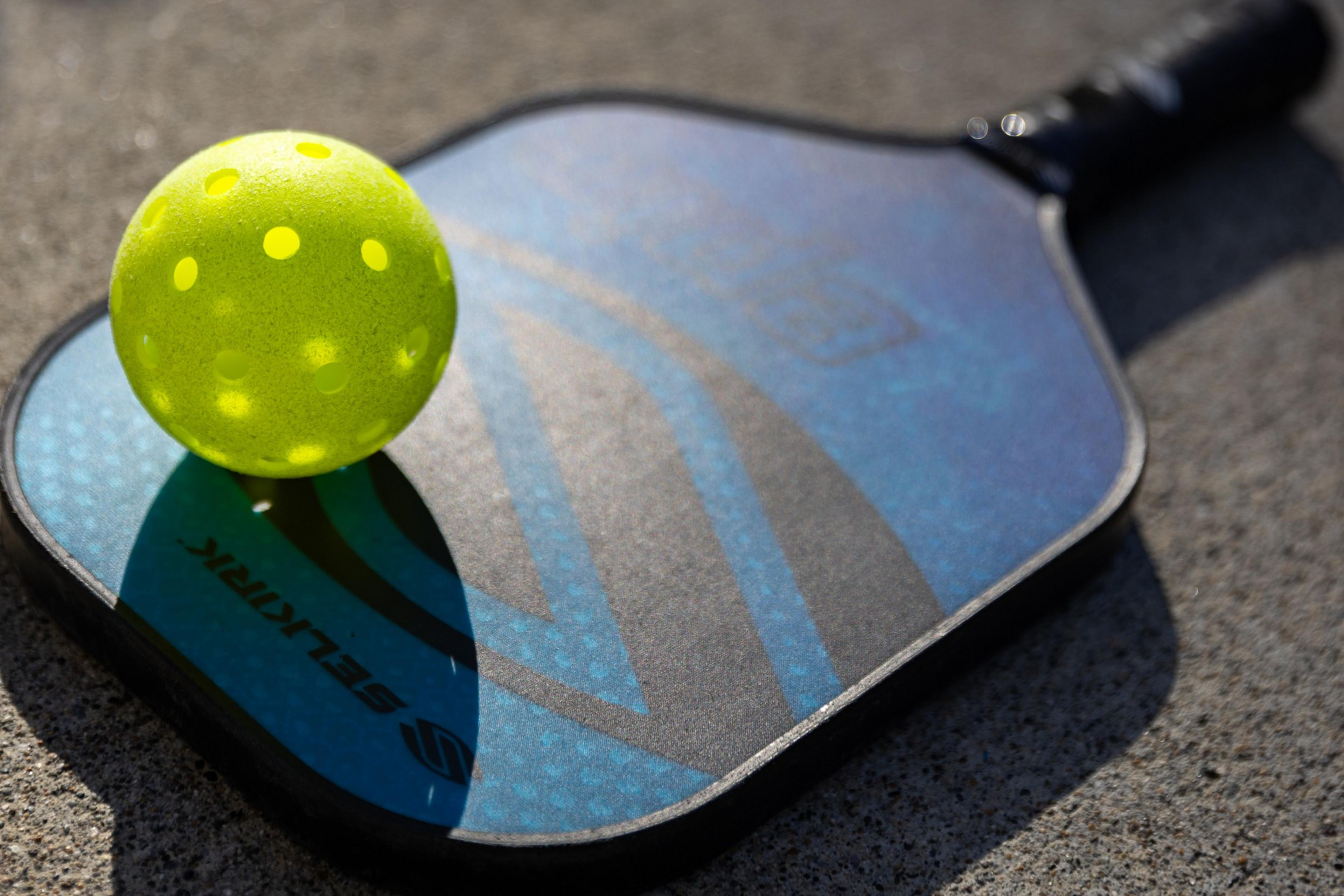 A yellow pickleball rests on a blue and black paddle on a textured ground.