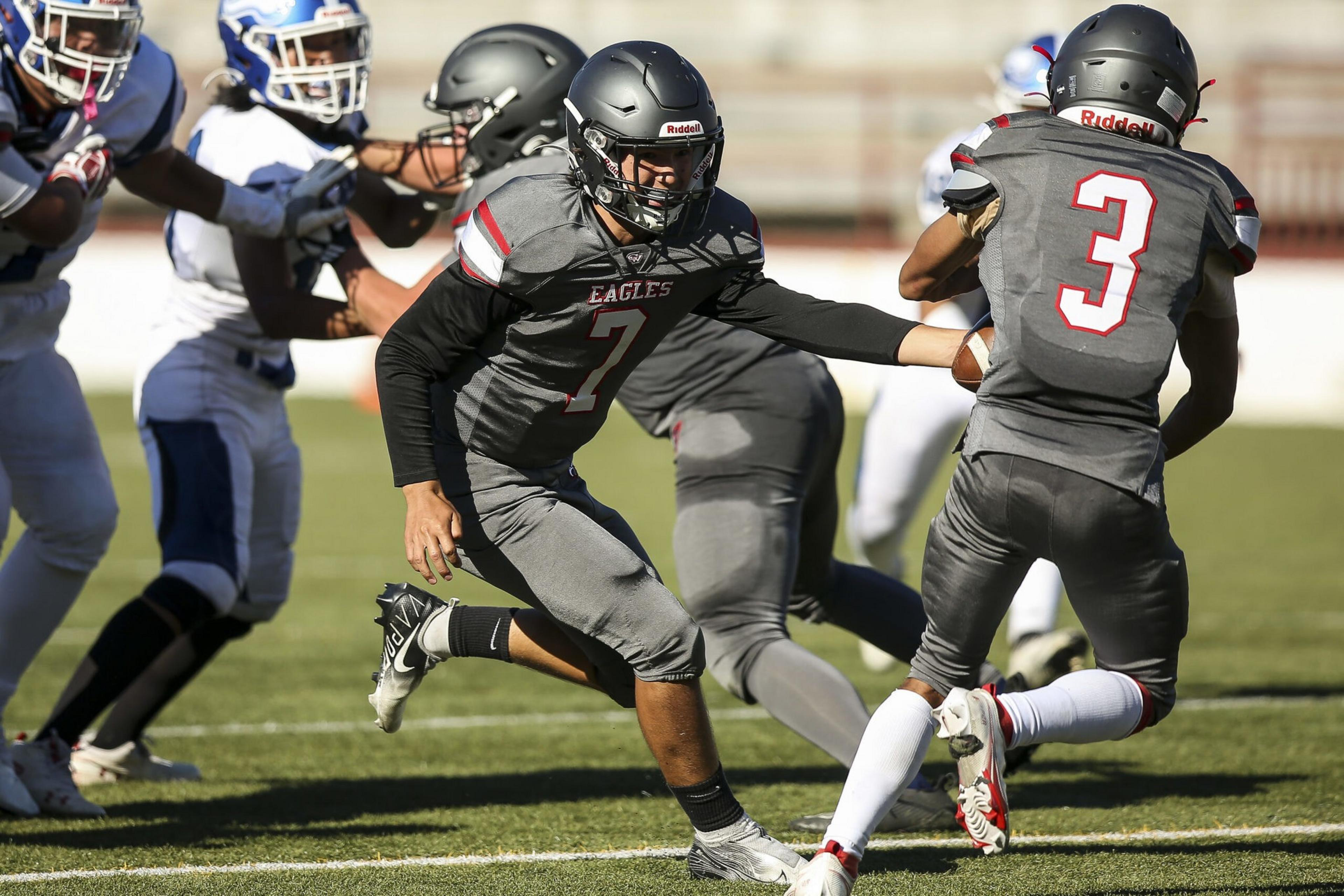 A football player wearing a gray Eagles uniform hands off the ball to a teammate with number 3 while opponents in white and blue rush in.