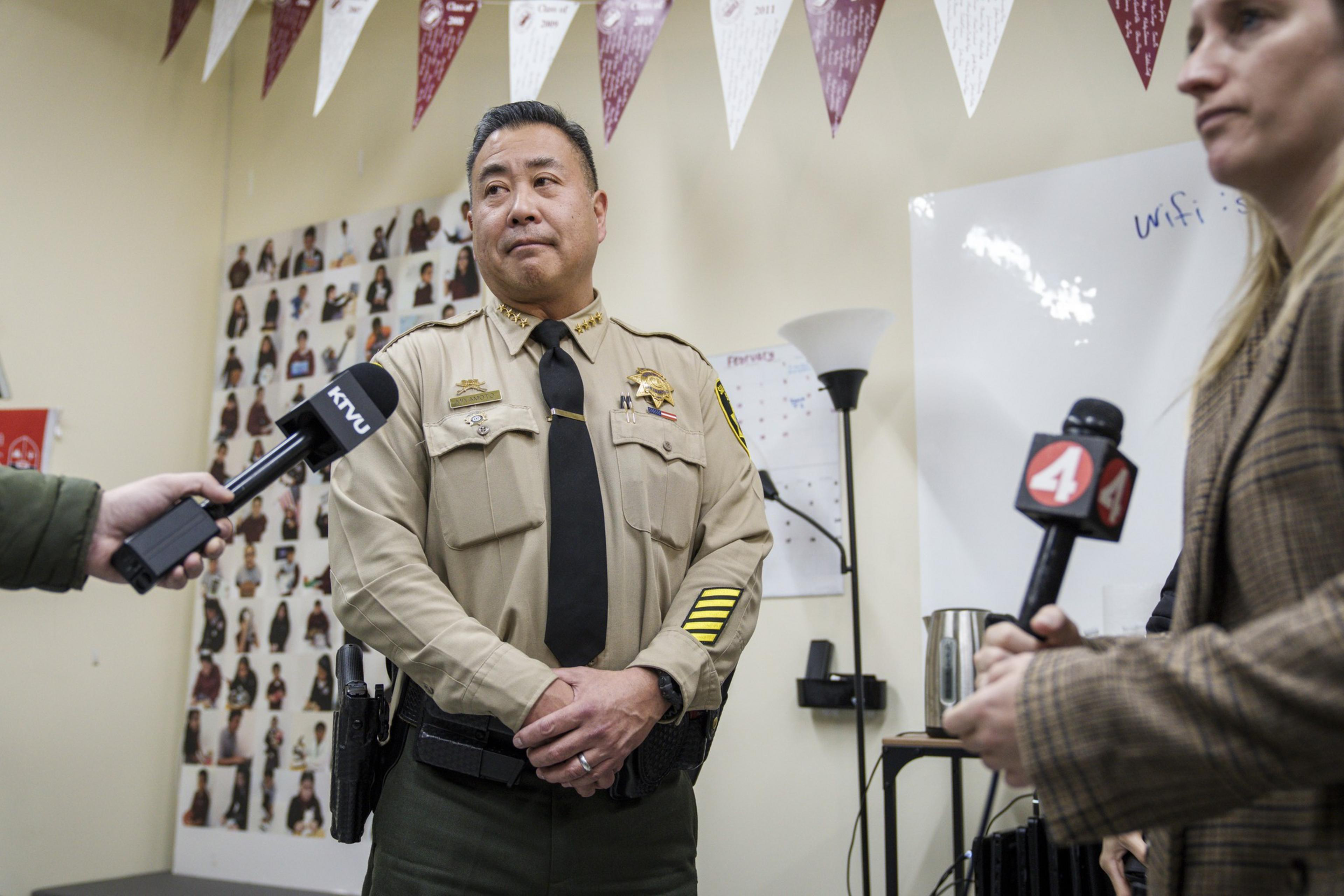Man in law enforcement uniform stands with hands clasped as person holds microphone in front of him