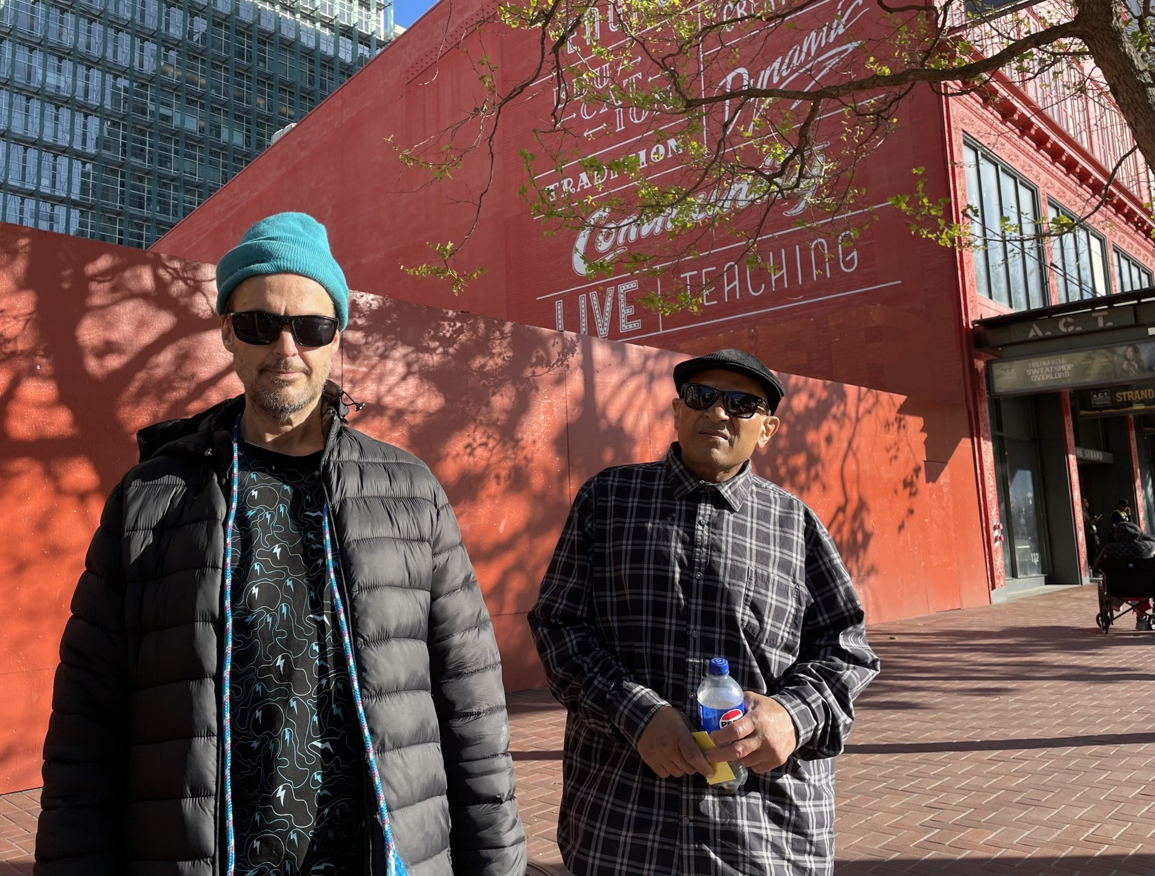 Two men stand on a sidewalk.