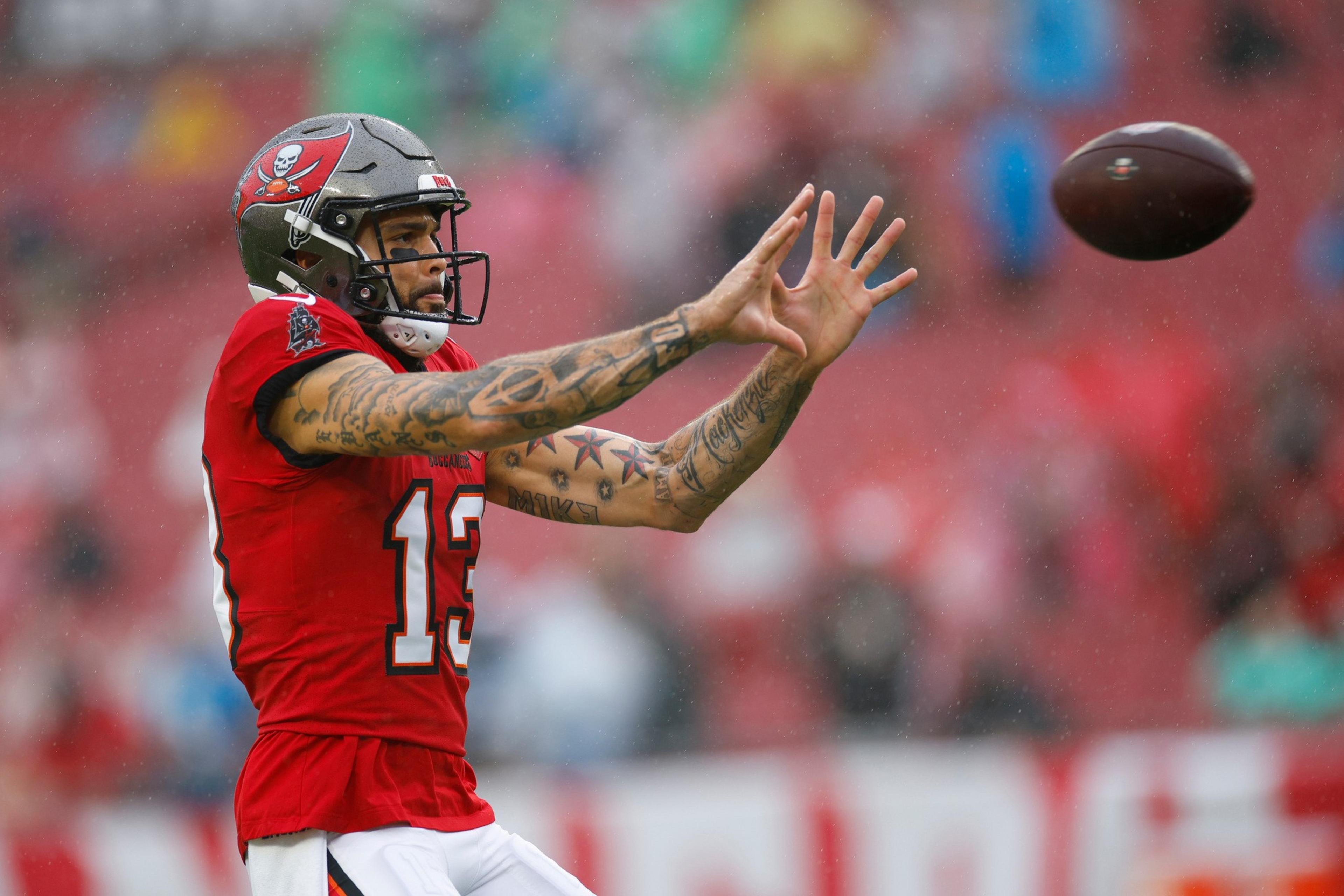 A football player wearing a red Tampa Bay Buccaneers jersey and helmet reaches out with both hands to catch a football in mid-air.