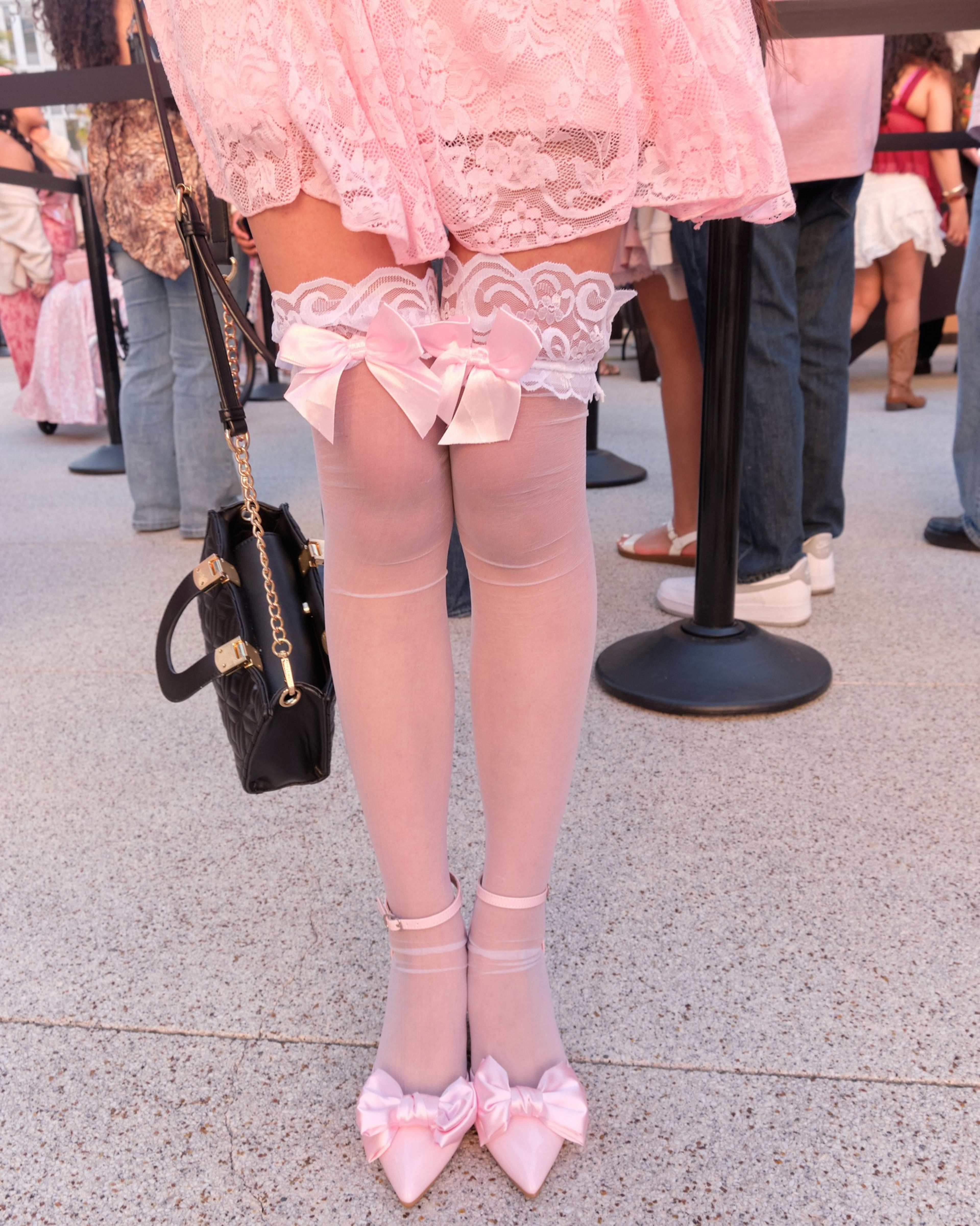 Pink lace stockings with bows are paired with pink pointed shoes adorned with matching bows, worn with a pink lace dress.