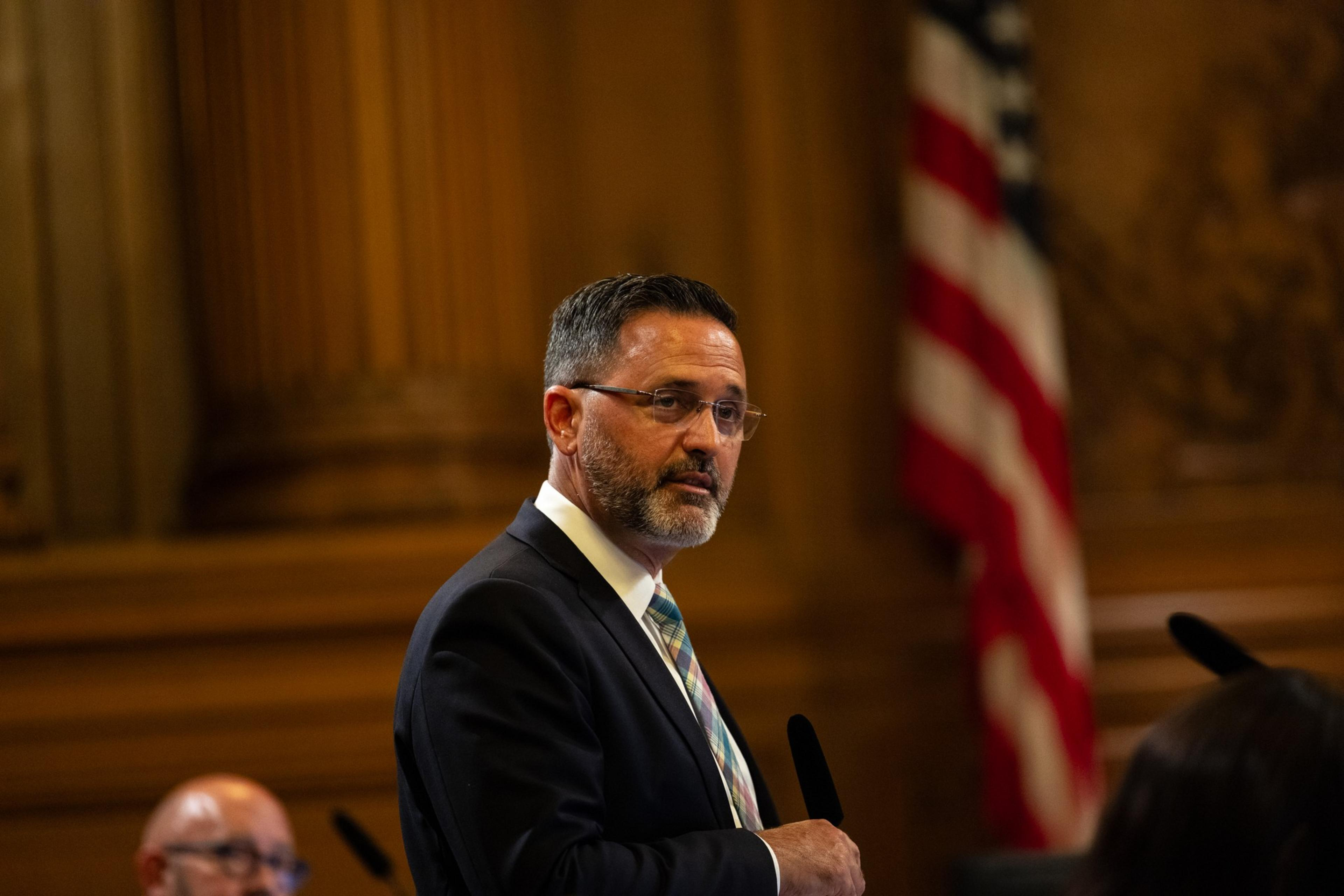Man in glasses speaks inside government building