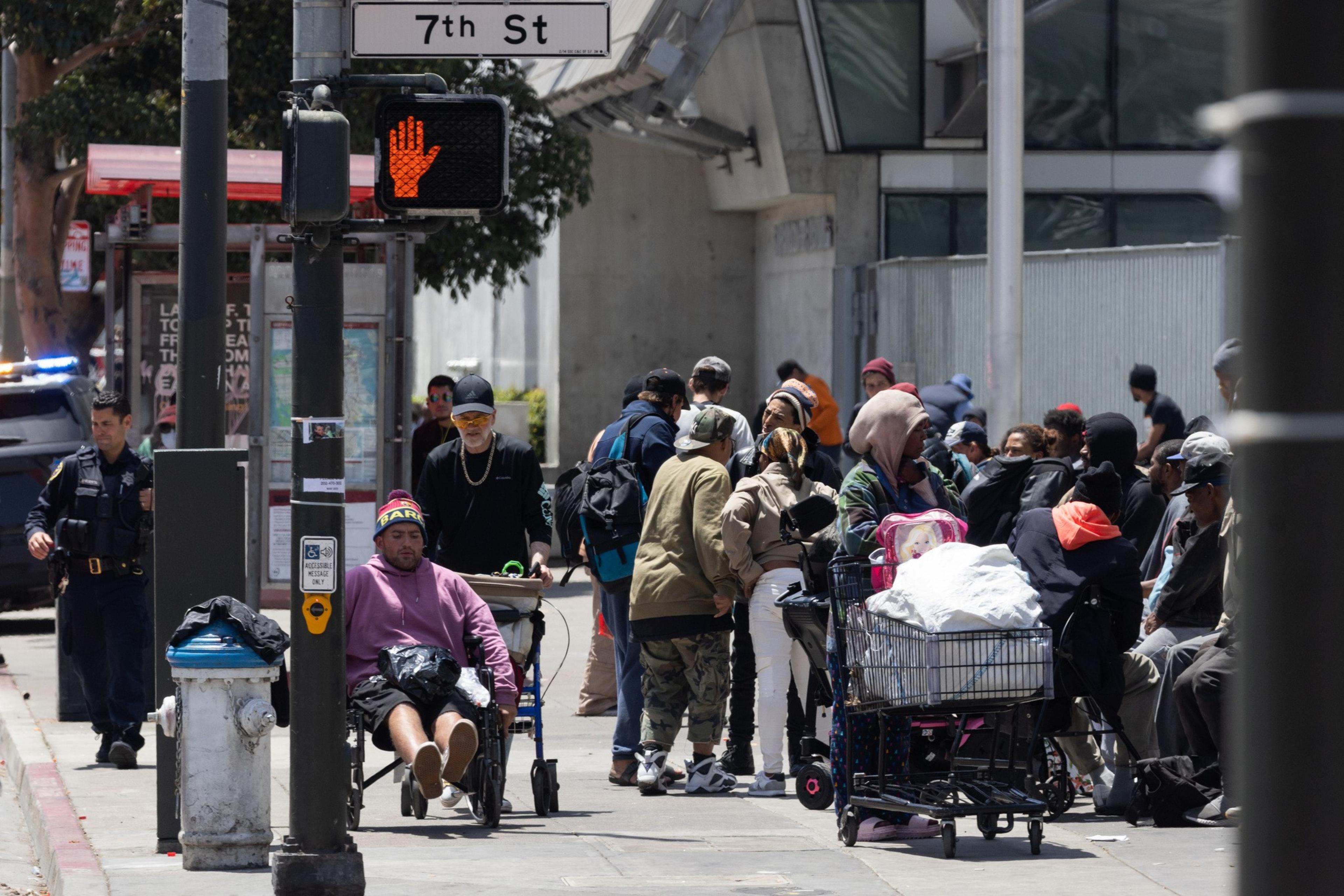 A group of people congregate on a street corner with a street sign that read 7th St.