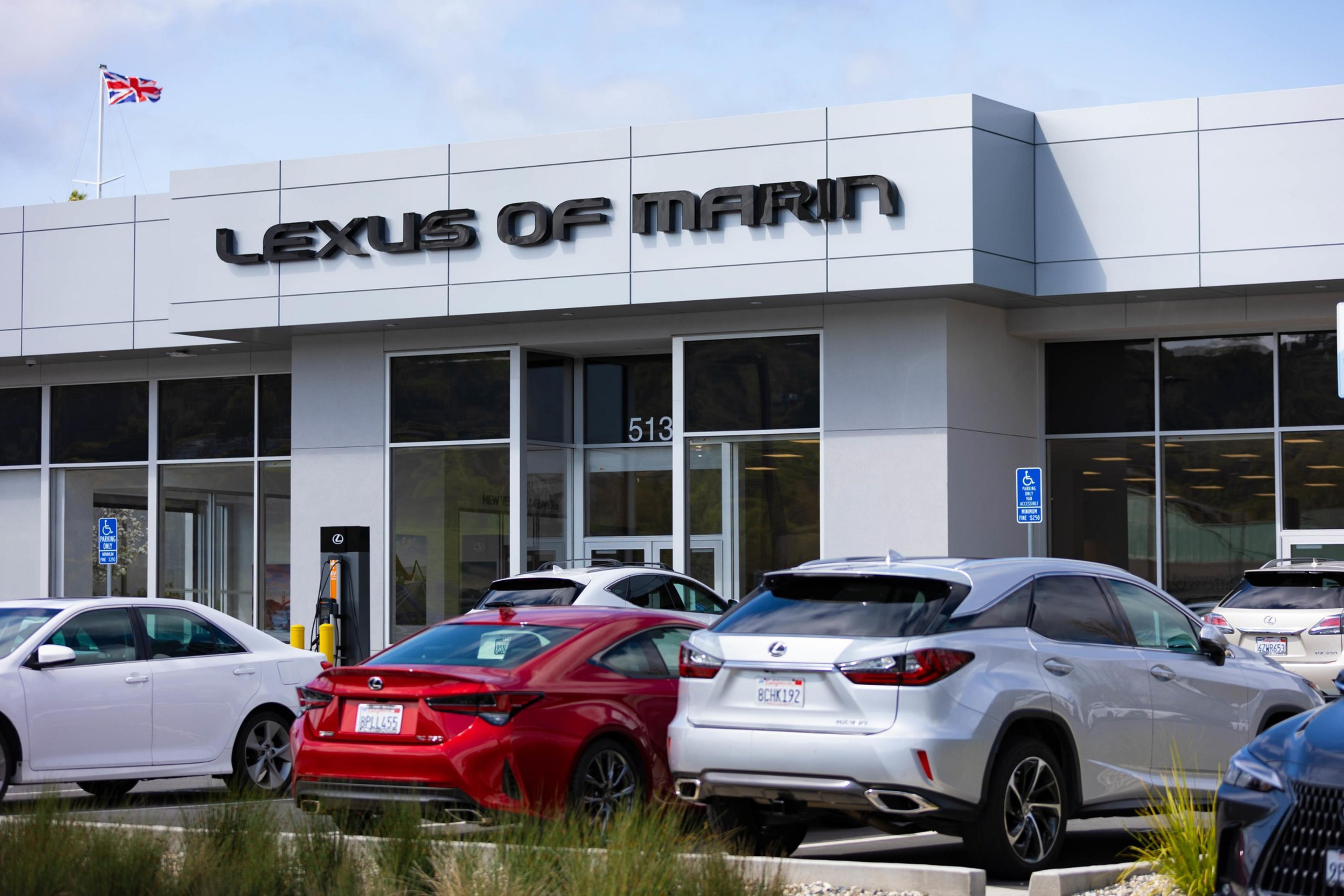 The image shows a Lexus dealership with several cars parked outside. The sign reads &quot;LEXUS OF MARIN&quot; above large glass windows and a door.