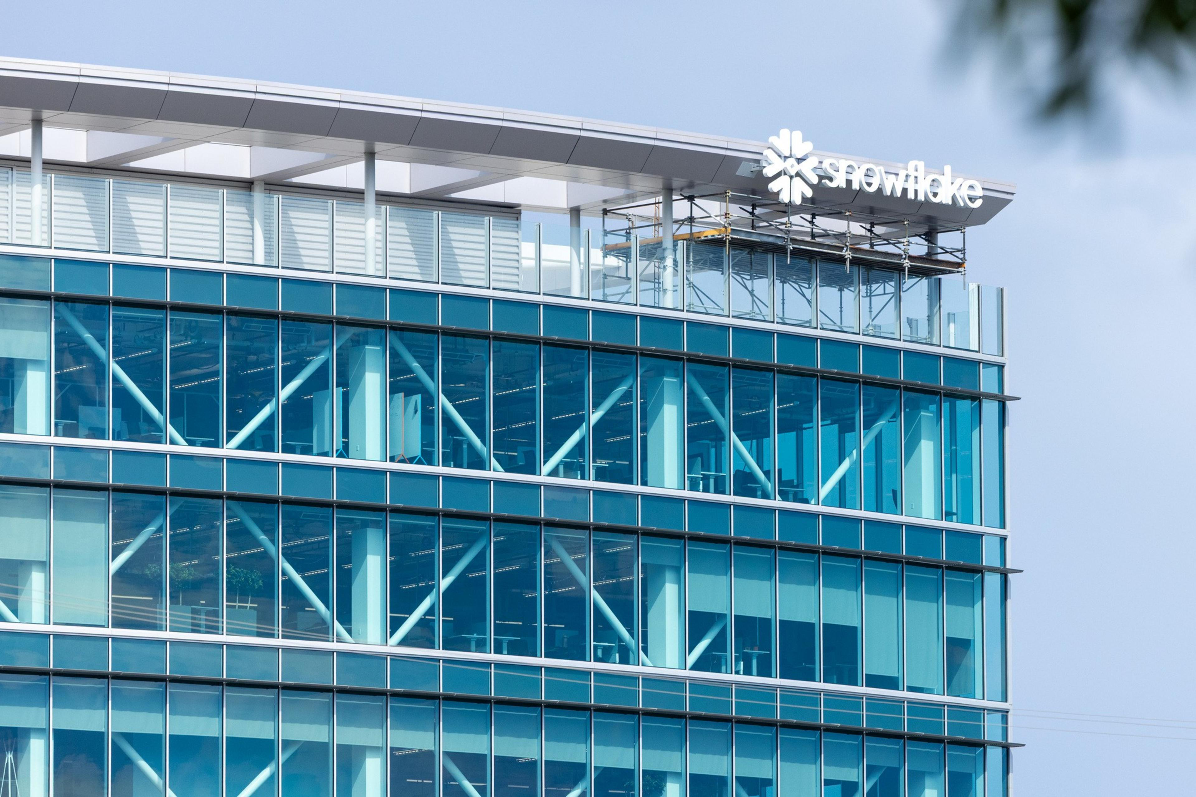 A modern office building with blue-tinted glass windows displays a "Snowflake" logo near the top corner under a curved white roof.