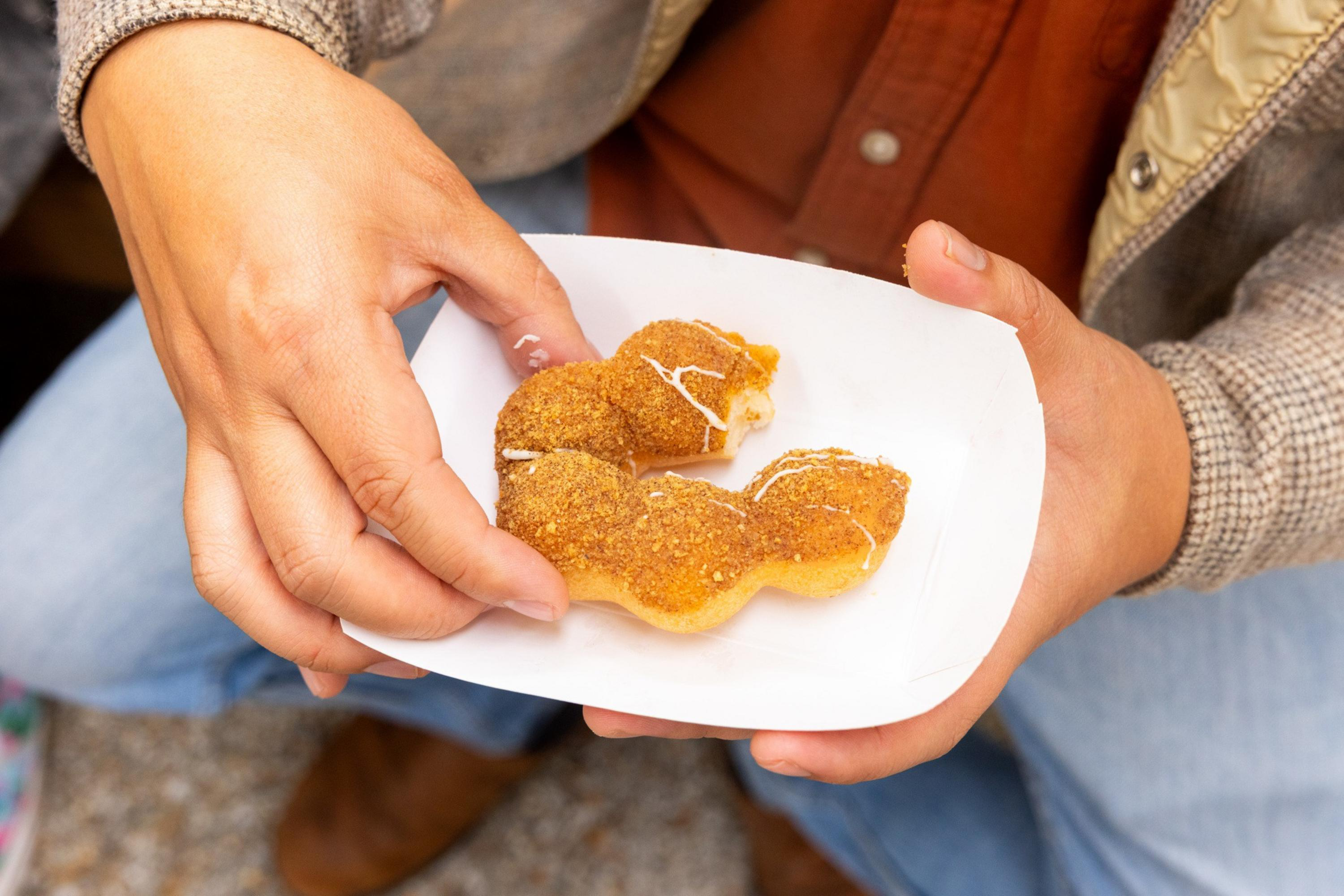 Two hands hold a white tray with a crescent-shaped, sugar-coated pastry partially drizzled with white icing.