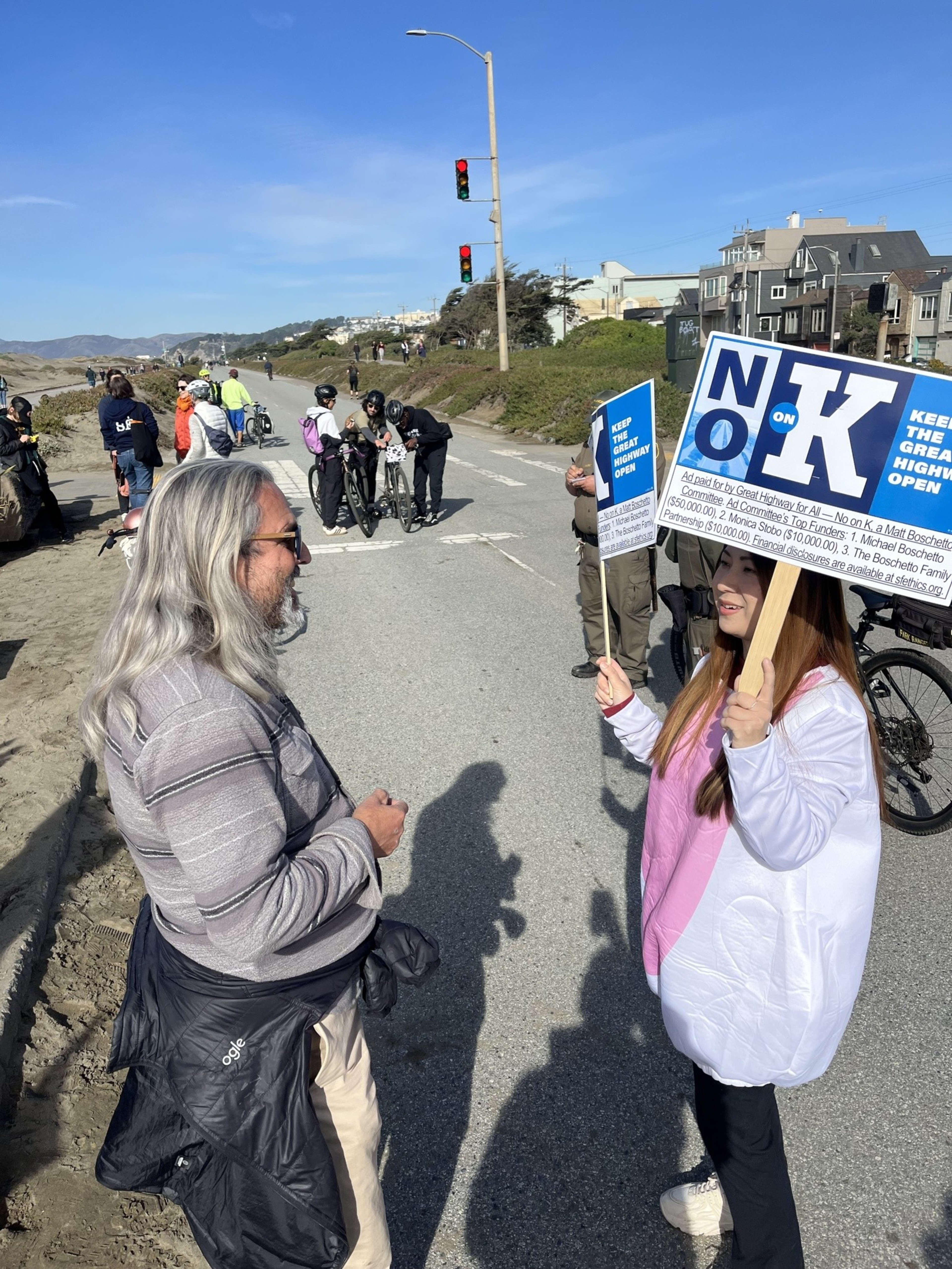 A man with long, white hair talks to a woman in a bunny costume on the Great Highway in San Francisco.