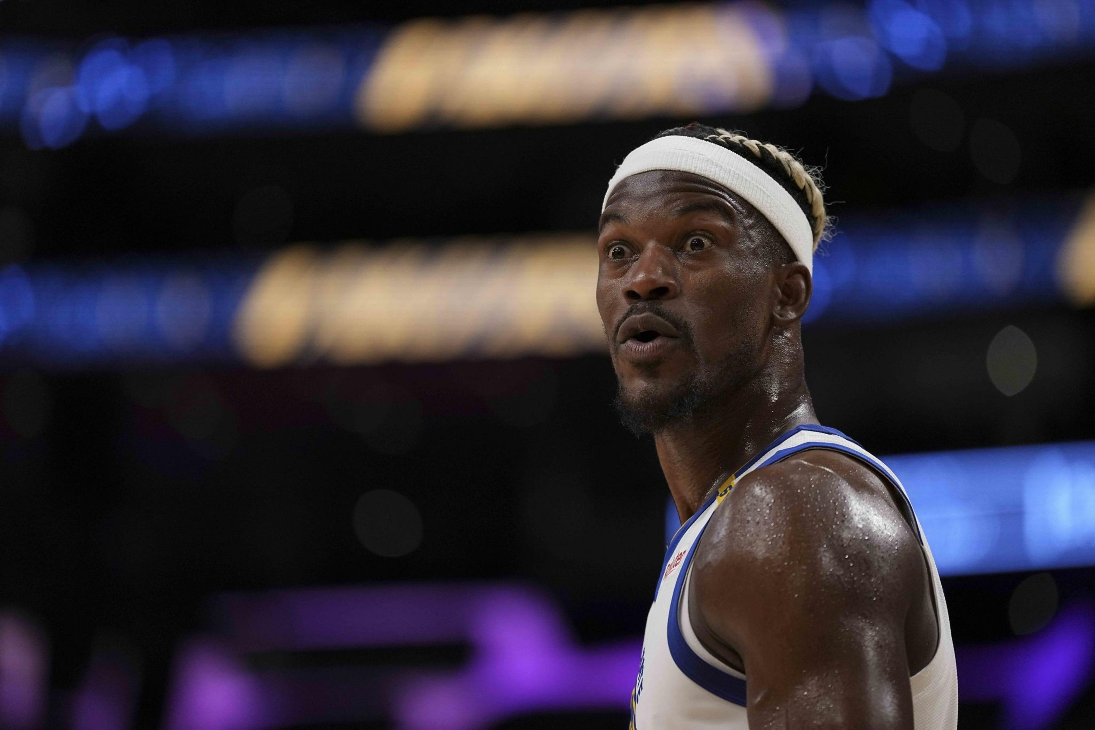 A basketball player with a white headband and jersey looks surprised. The background is blurred with purple and blue tones, focusing attention on his expression.