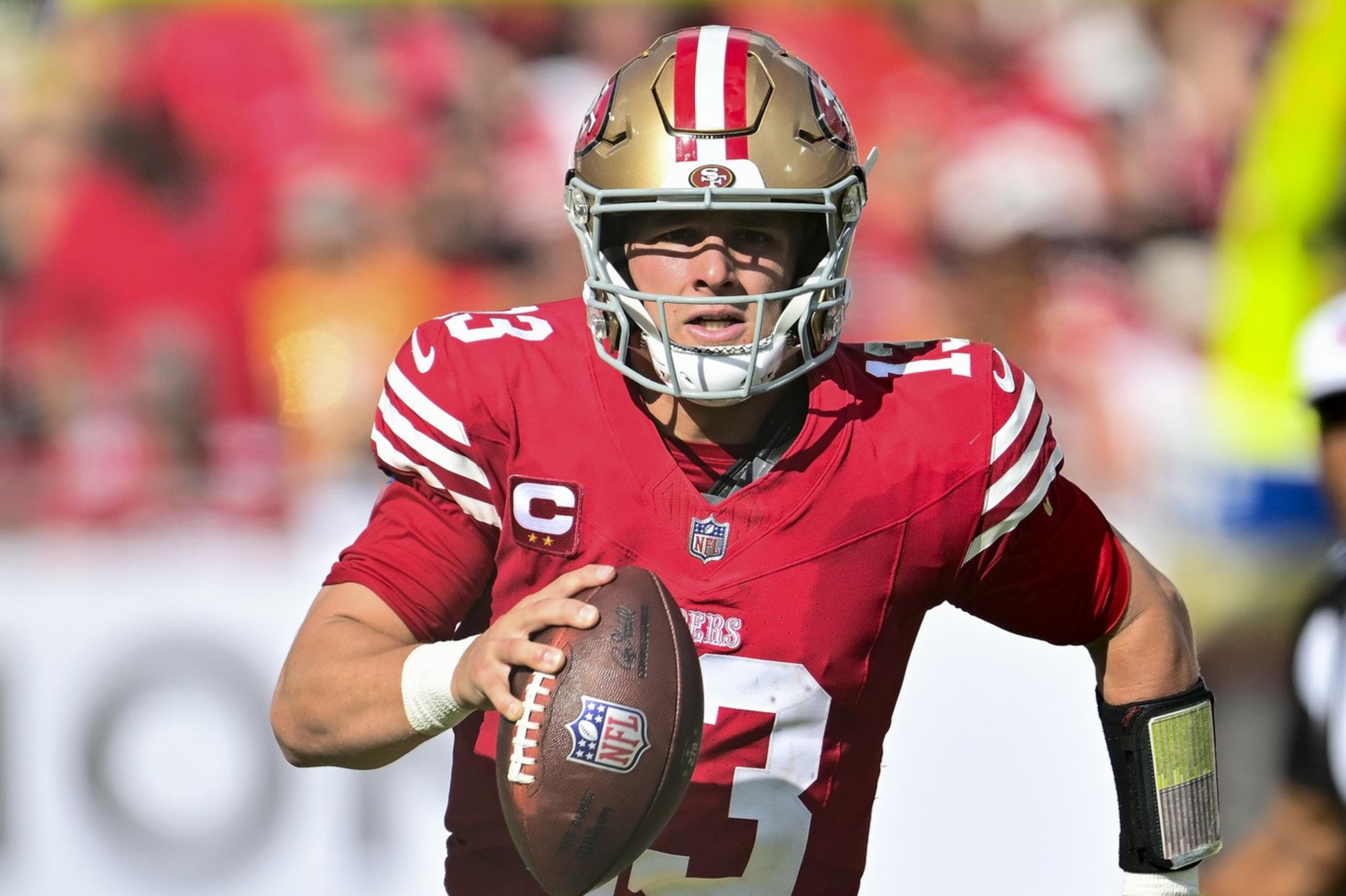 A football player in red and gold uniform runs on the field, holding the ball. He's wearing a helmet, and sunlight shines on him, creating a dynamic action scene.