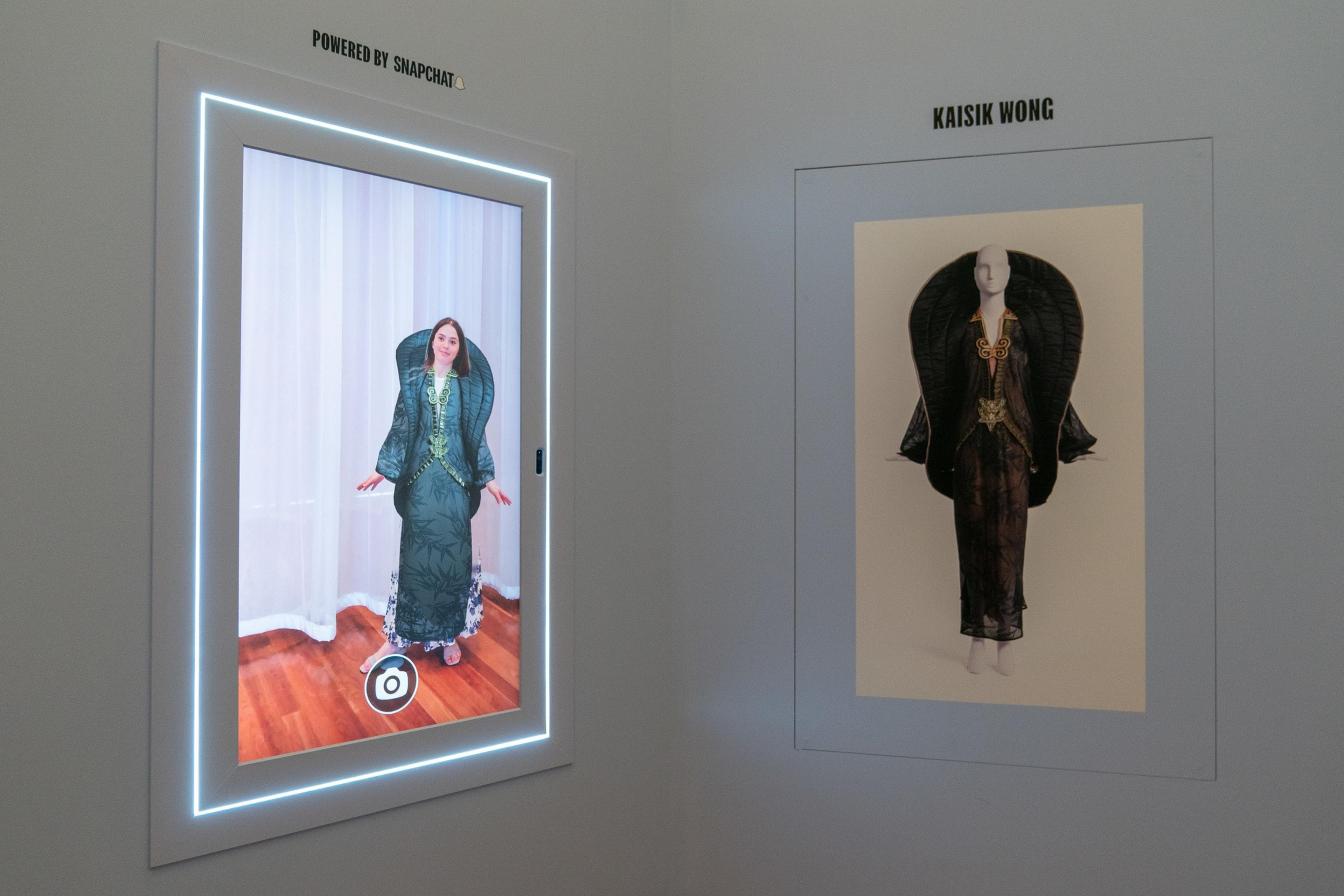 A person in a green elaborate dress appears on a screen, with the dress in a photograph beside it. 
