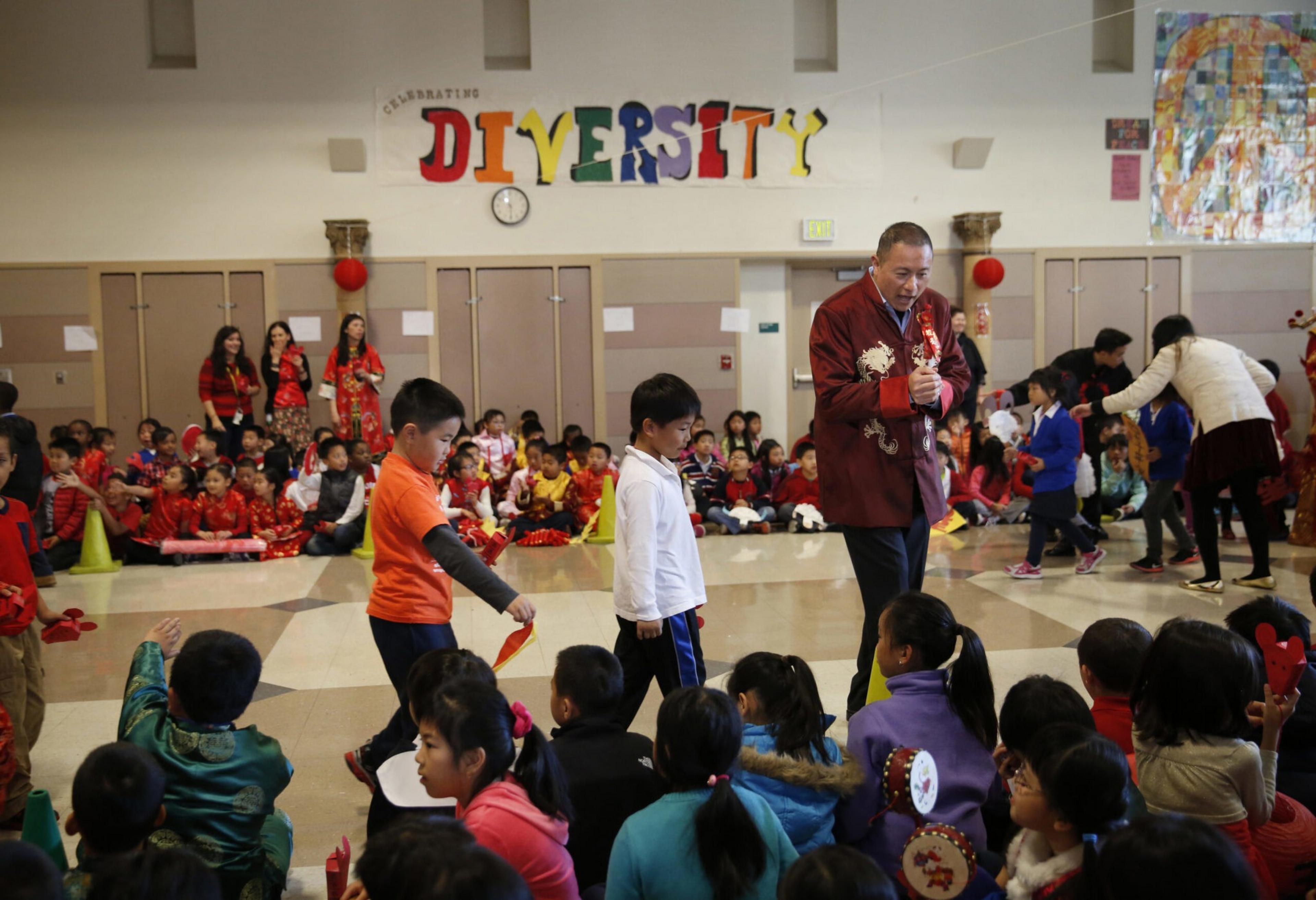 Children and adults gather in a school gym decorated with a colorful "DIVERSITY" sign, engaging in an event with traditional and casual clothing.