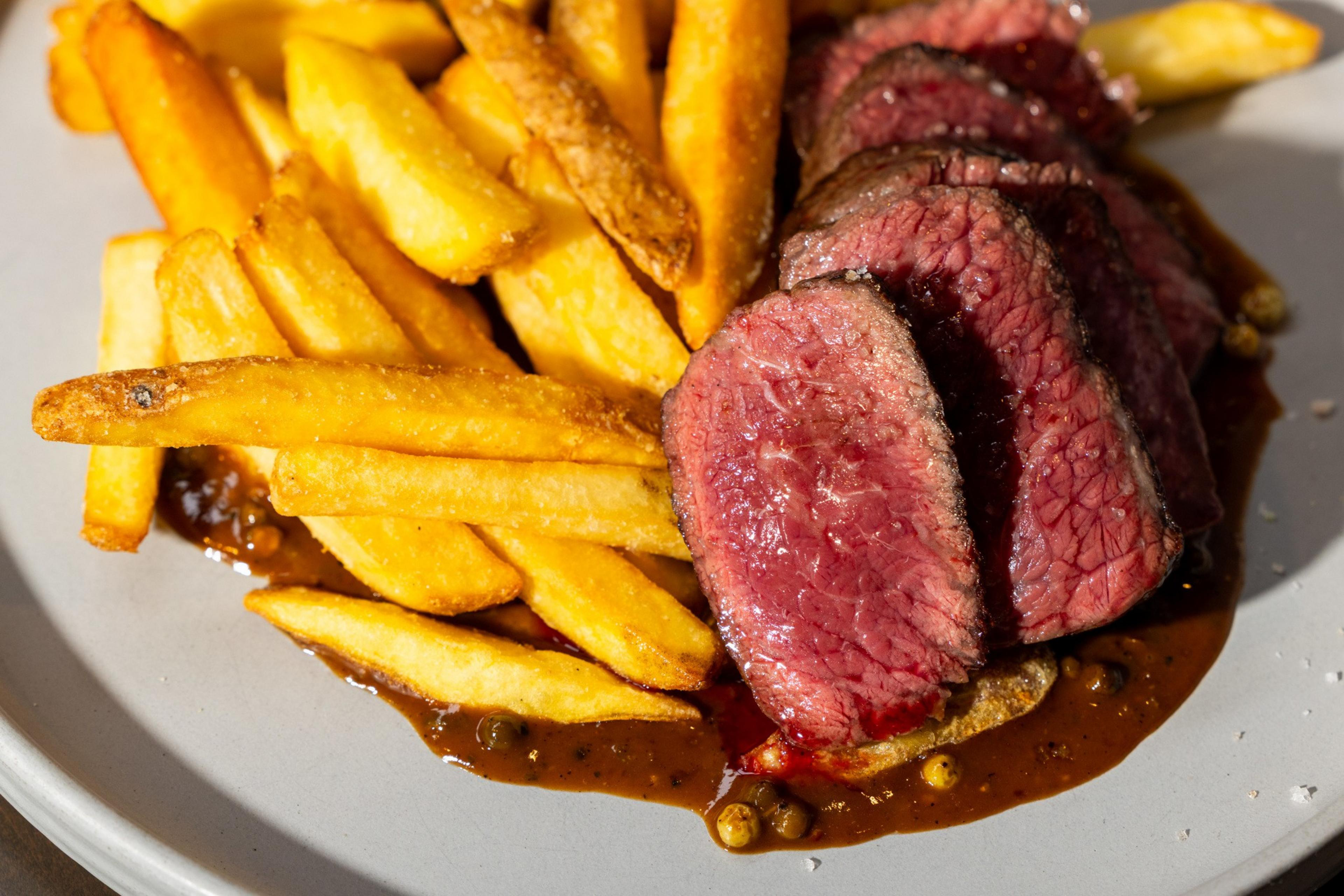 Thick-cut golden fries served alongside medium-rare slices of beef on a plate with a rich, dark peppercorn sauce.