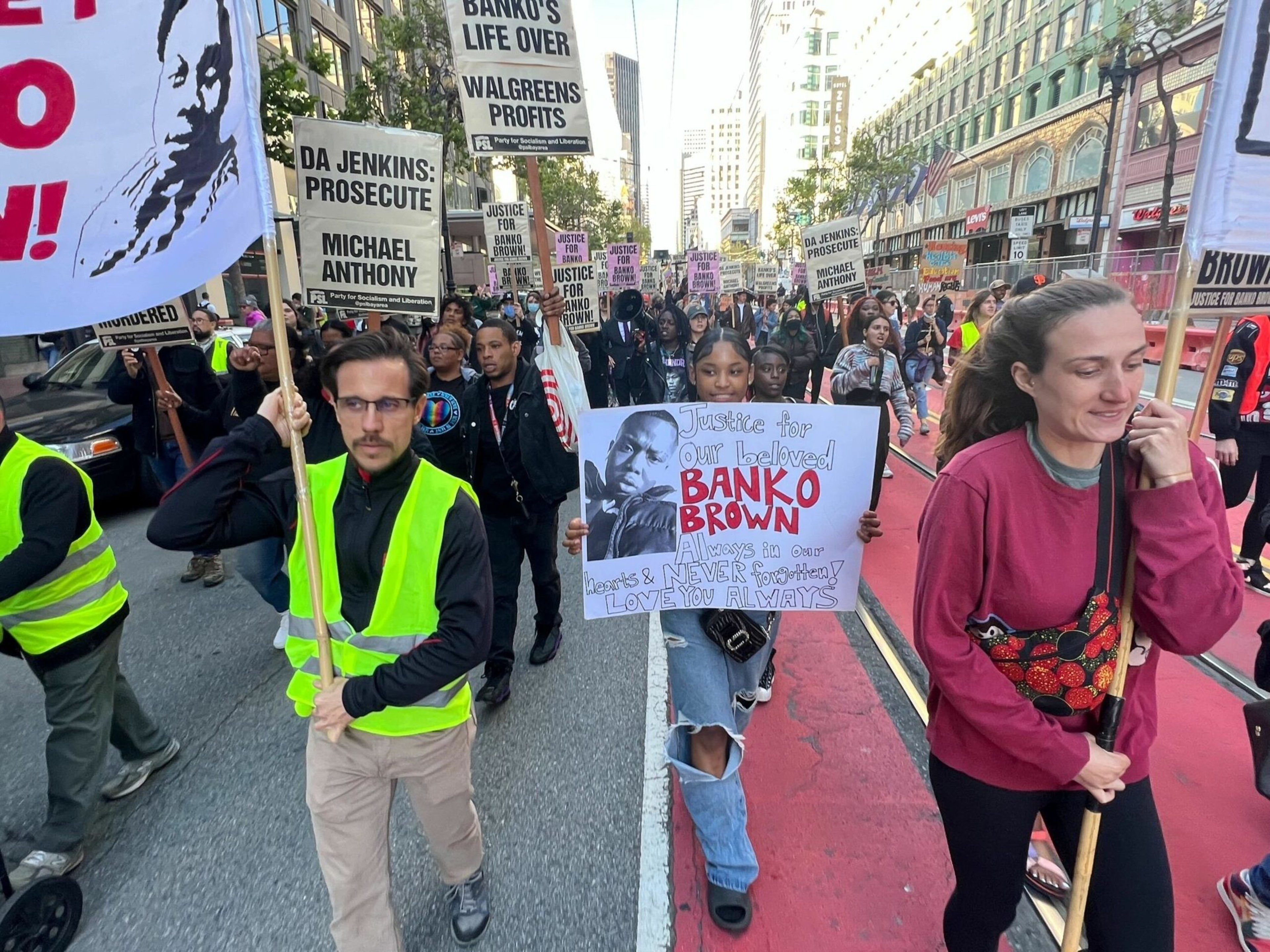 A group of protestors march on a city street holding signs demanding justice for Banko Brown and prosecution for DA Jenkins.