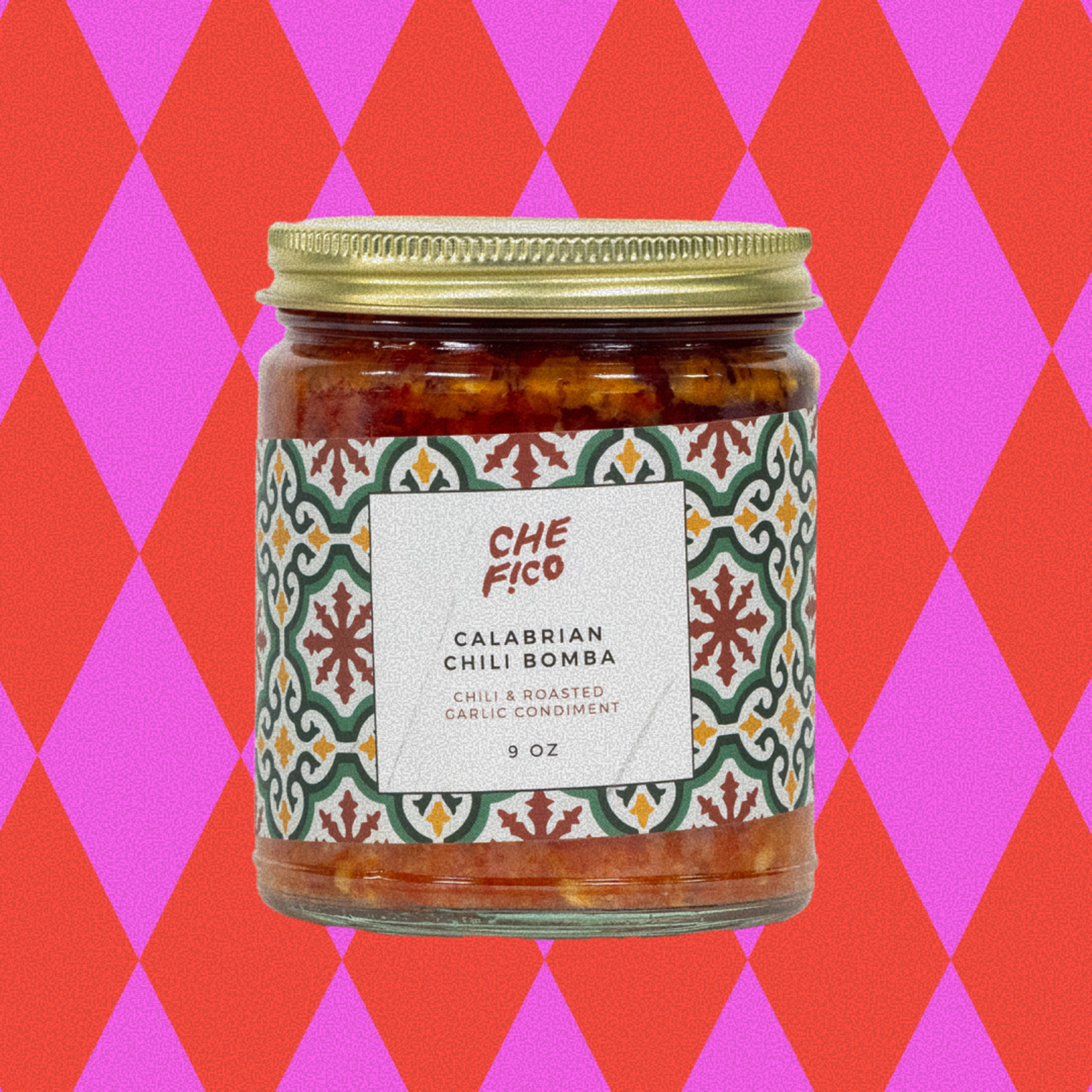 A glass jar with a gold lid contains Che Fico Calabrian Chili Bomba, a chili and roasted garlic condiment, weighing 9 ounces.