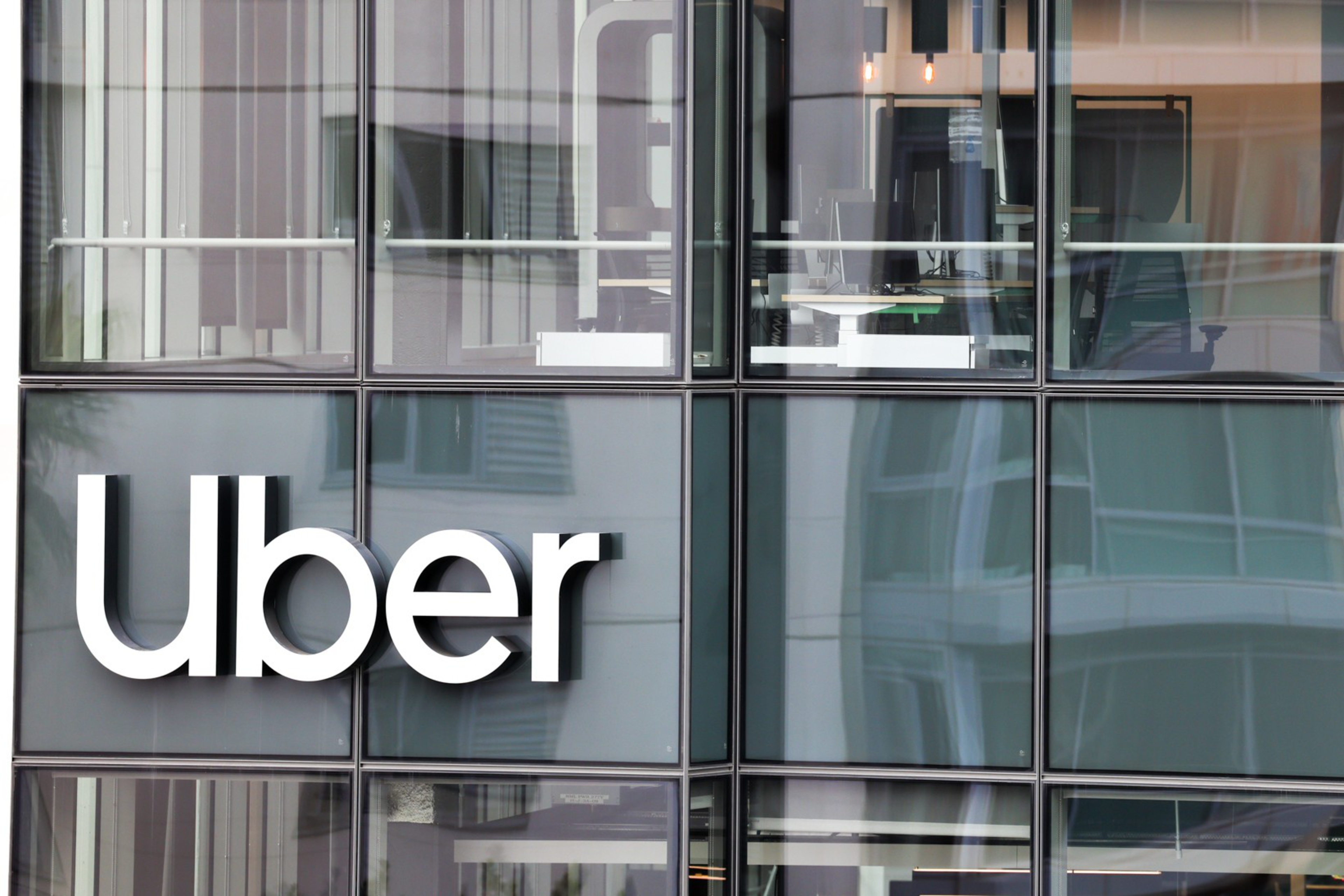 The image shows the large "Uber" logo on the exterior of a modern building with glass facade and reflections.