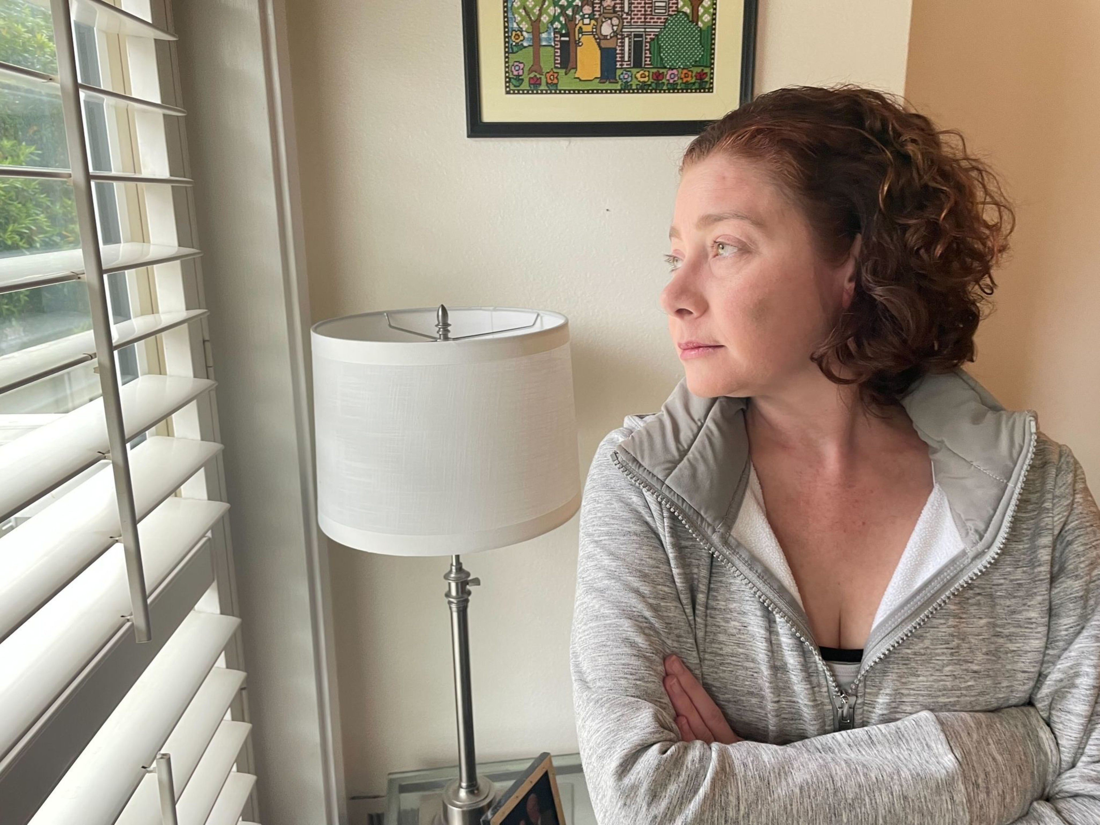 A woman stands in front of a window.