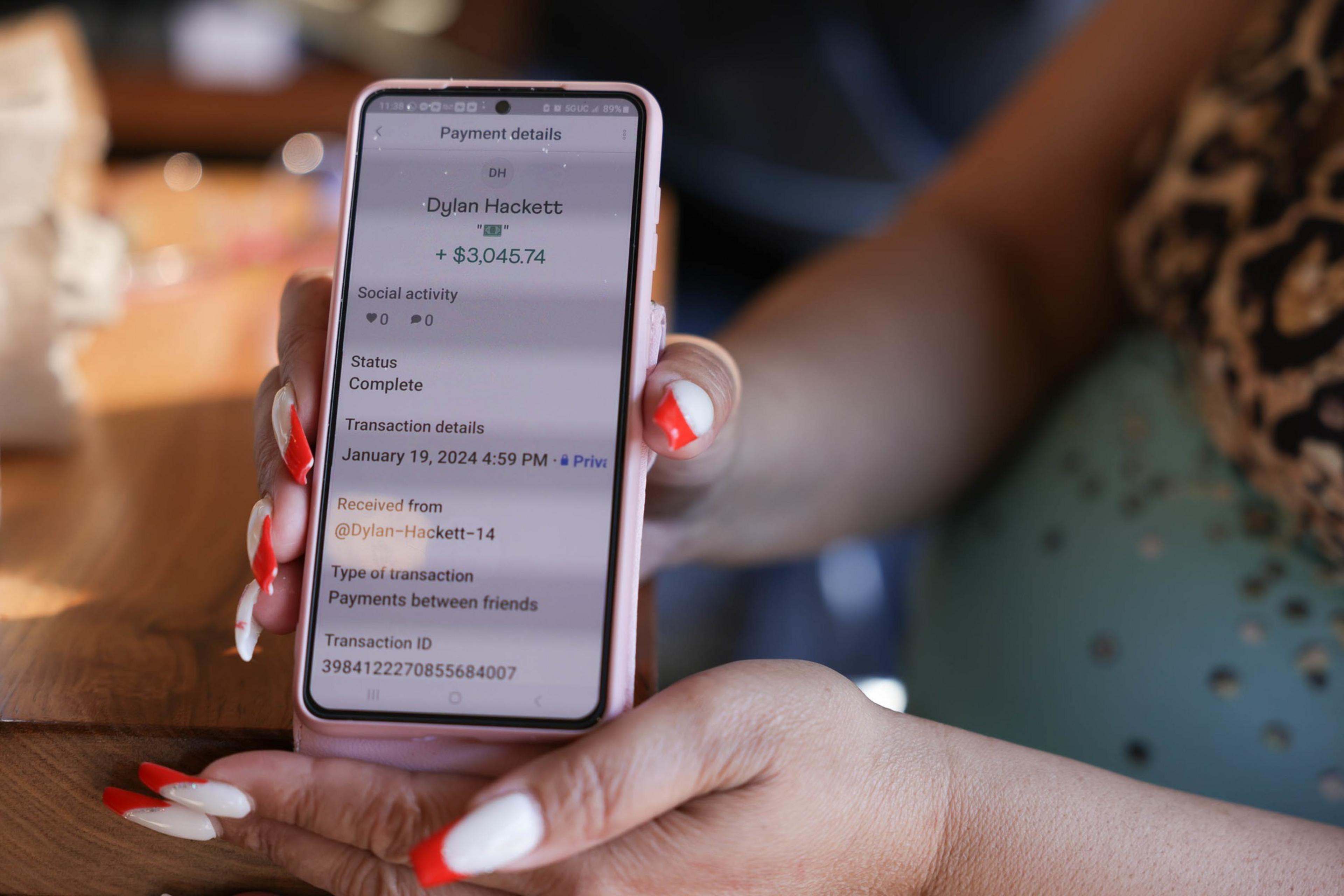 A person holds a phone displaying a payment receipt of $3,045.74, marked complete, from someone named Dylan Hackett.