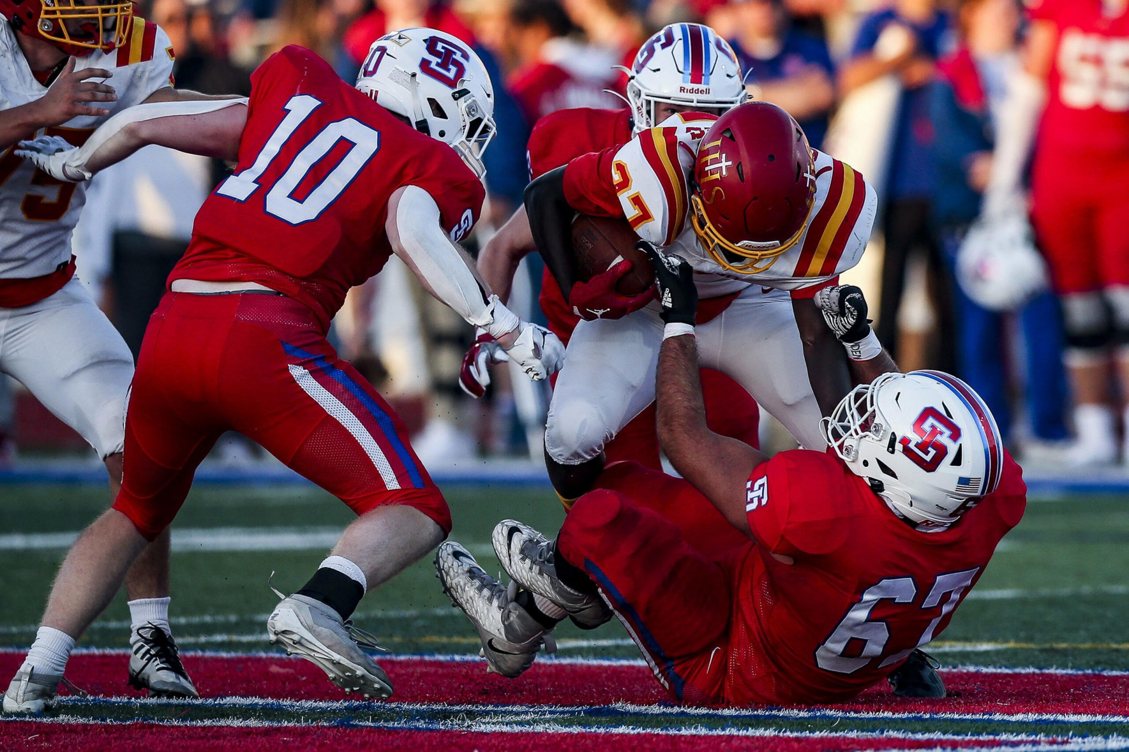 A football player in a red and yellow uniform is tackled by two players in red and white uniforms during an intense play on the field.