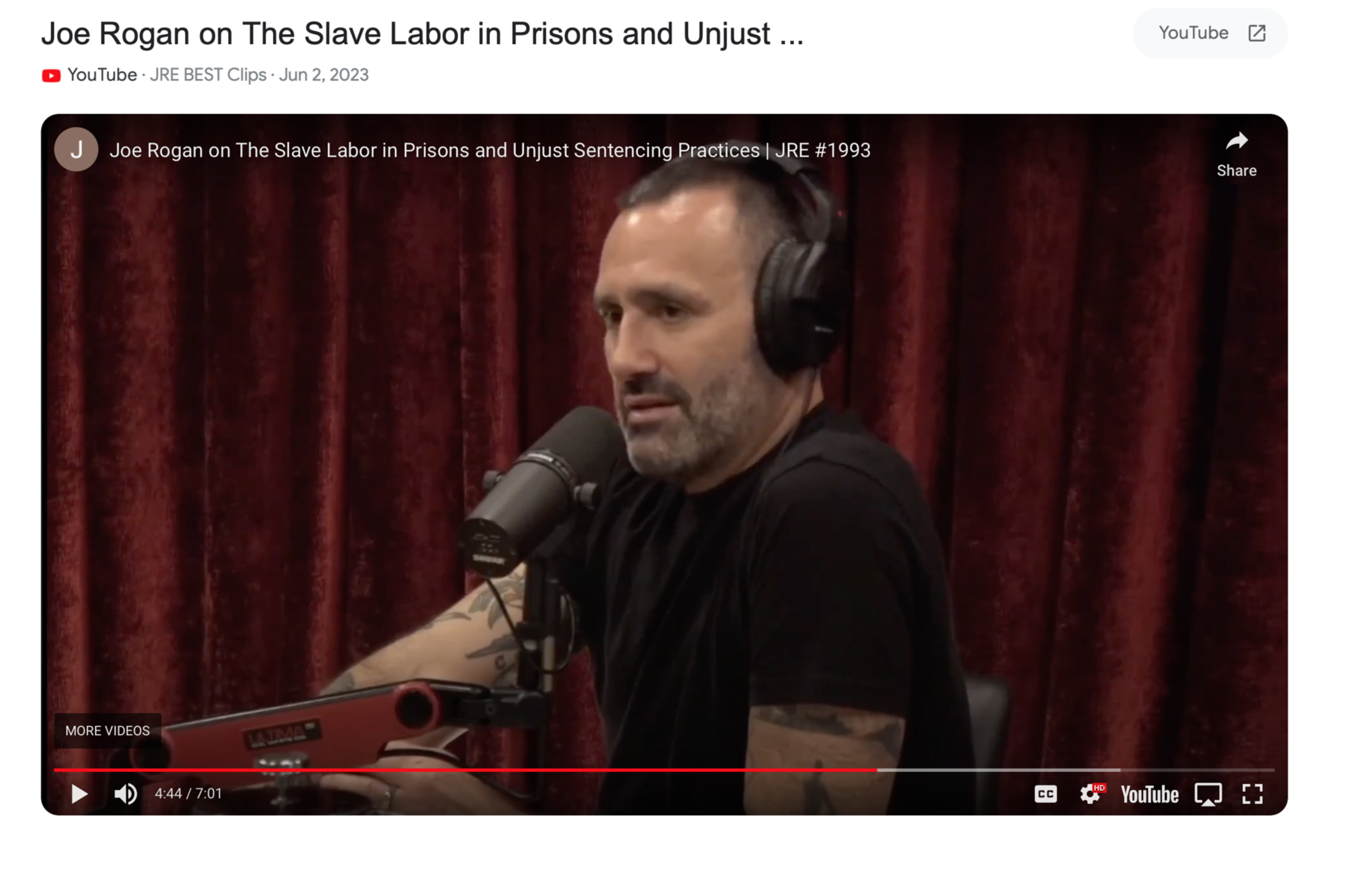 A man with short dark hair and a beard wears headphones and speaks into a microphone, seated against a dark red curtain.