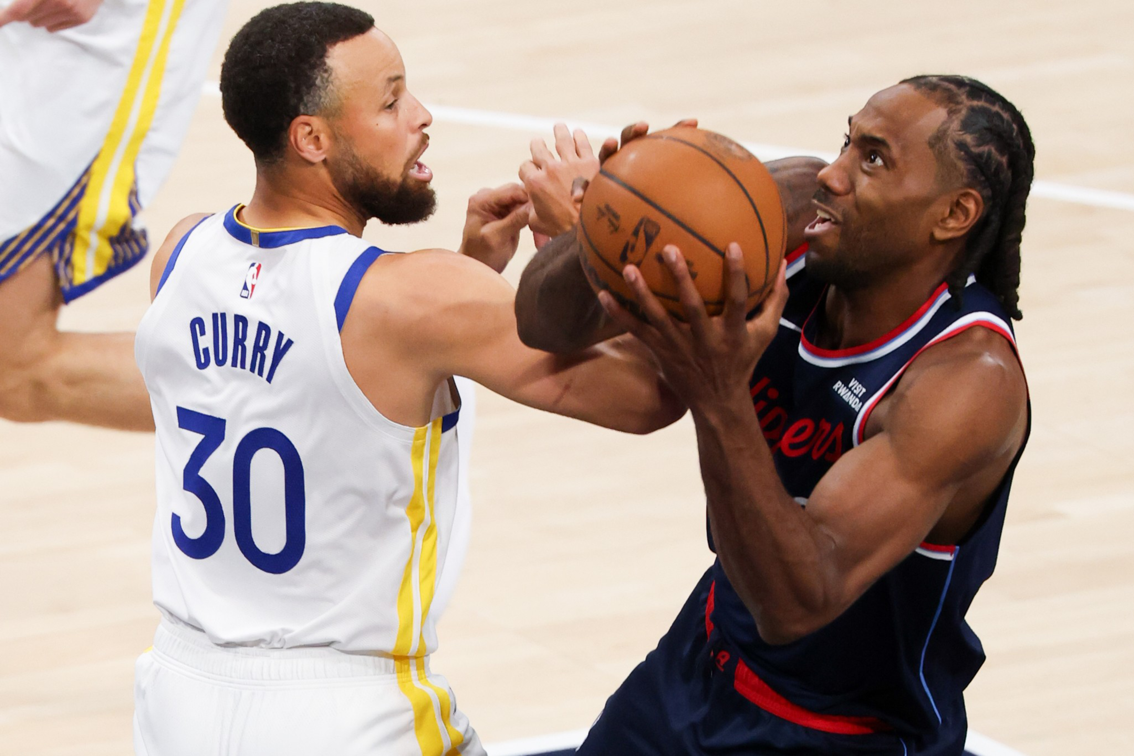 A basketball player in a dark blue uniform with braids grips the ball tightly while being closely defended by a player in a white jersey numbered 30.