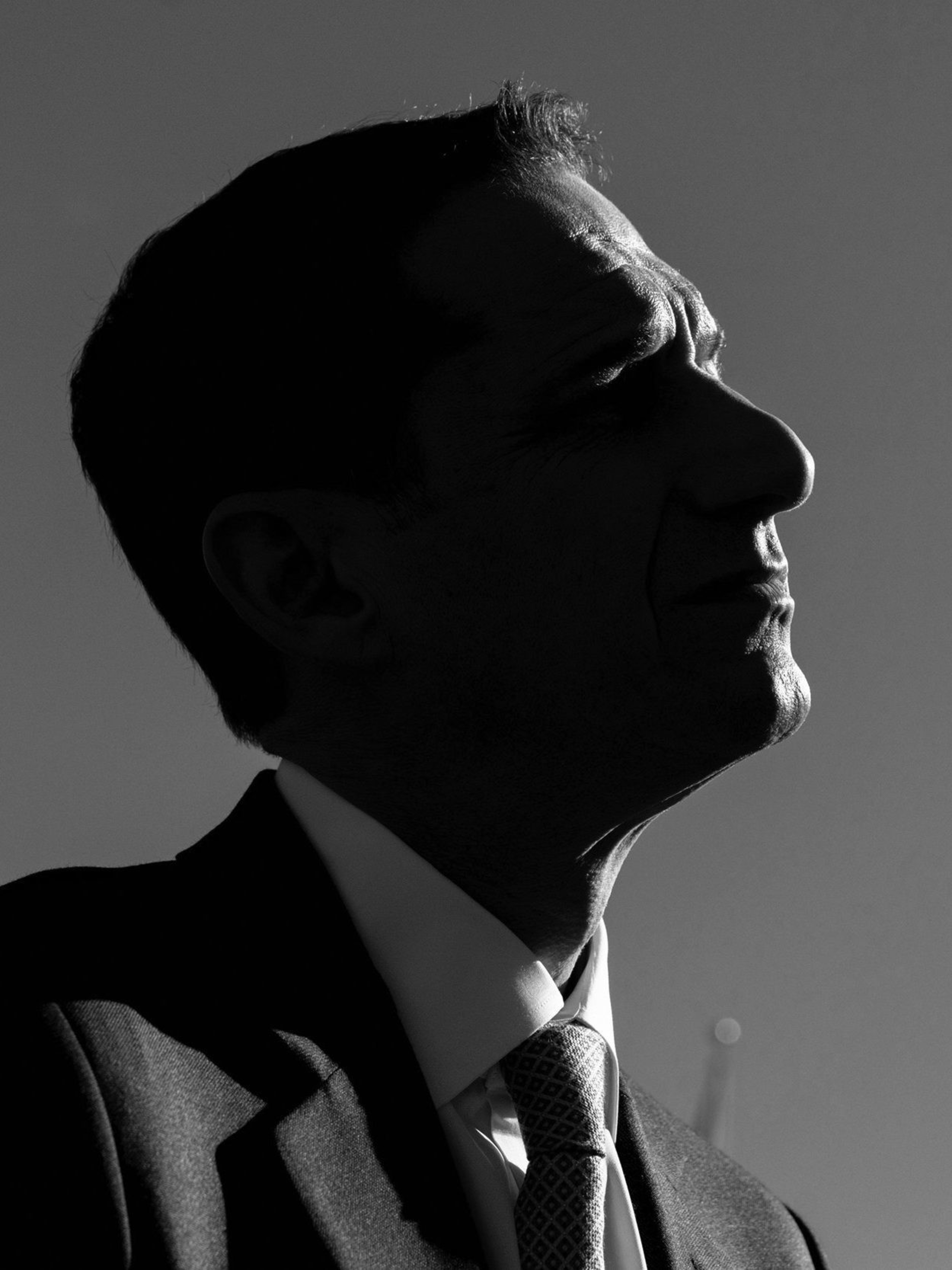 A silhouette of a man in a suit and tie is shown against a plain background, his face in profile, looking upward with distinct shadows highlighting his features.