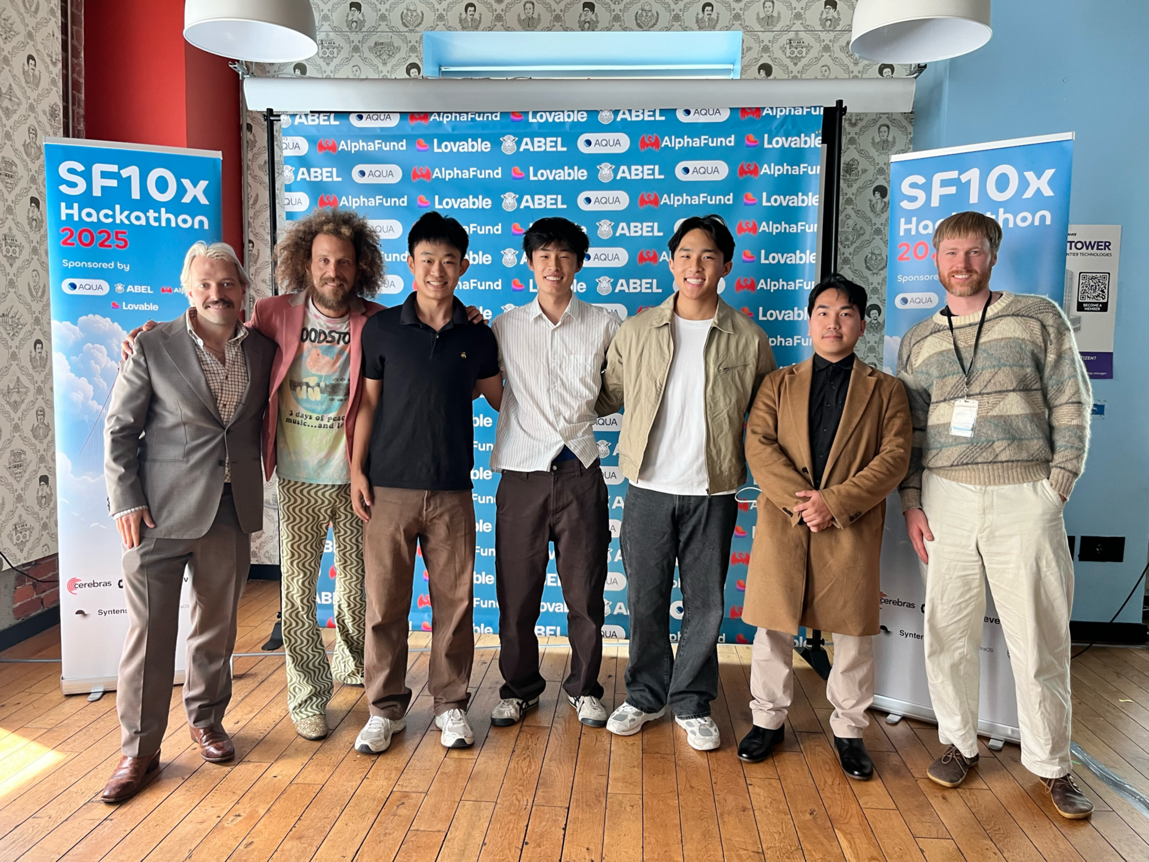 Seven men stand side by side on a wooden floor in front of a blue backdrop with logos, flanked by two banners for the SF10x Hackathon 2025 event.