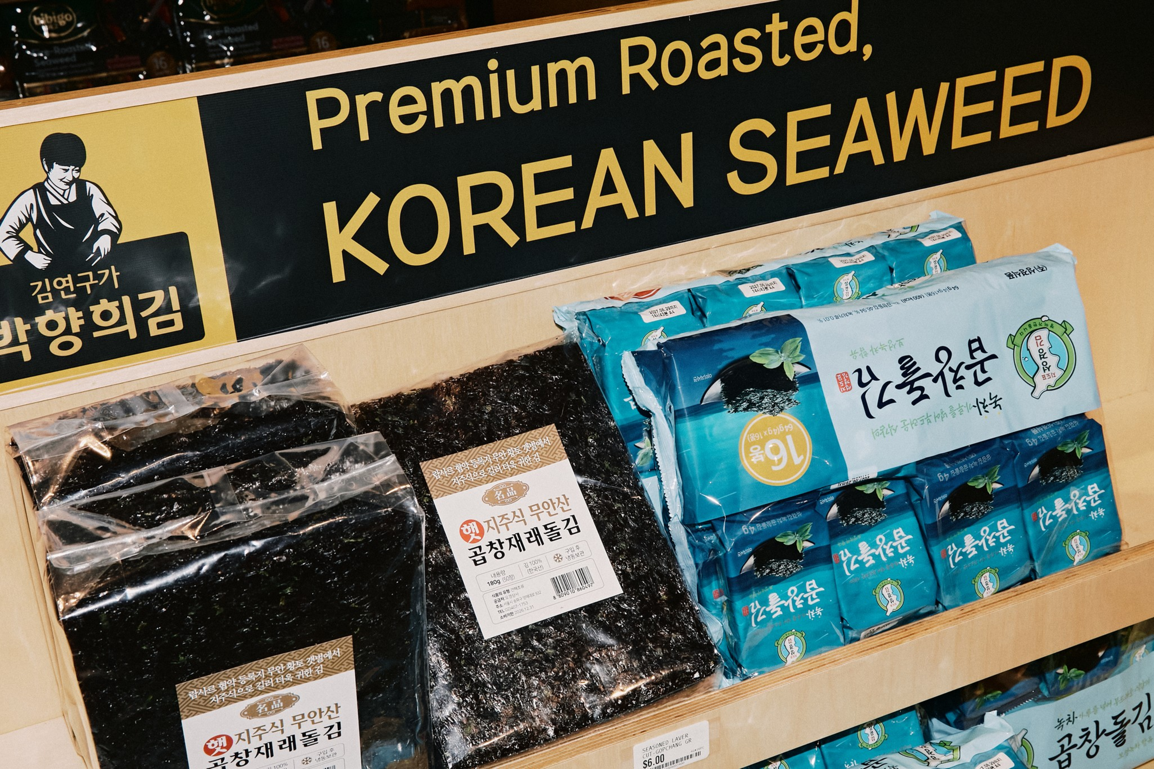Packages of premium roasted Korean seaweed are displayed on a wooden shelf under a sign with bold yellow text.
