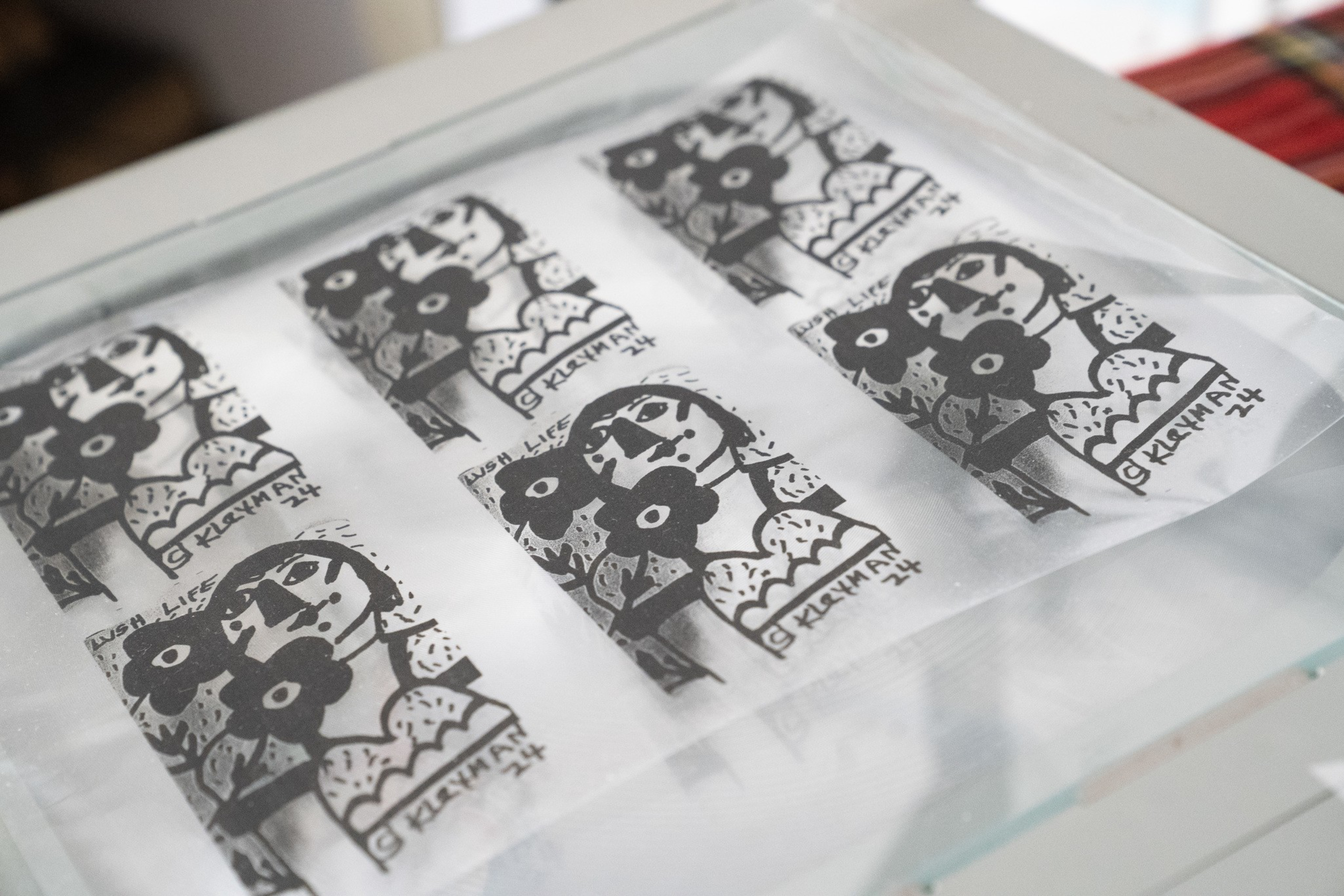 Six black and white prints of a stylized face with flowers and patterns are arranged on a flat surface under glass.