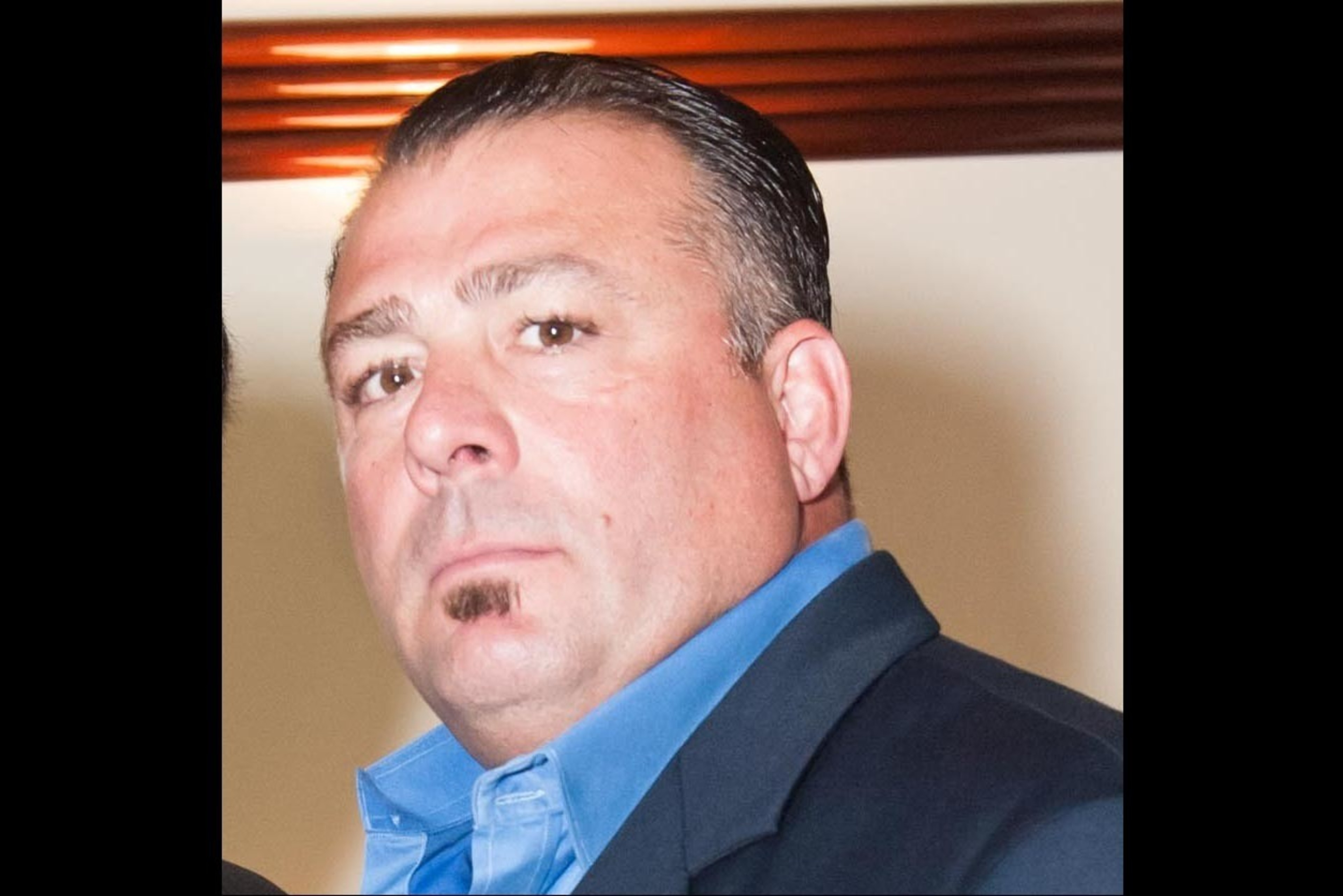 A man with a neat haircut, wearing a blue shirt and dark jacket, looking slightly off-camera.