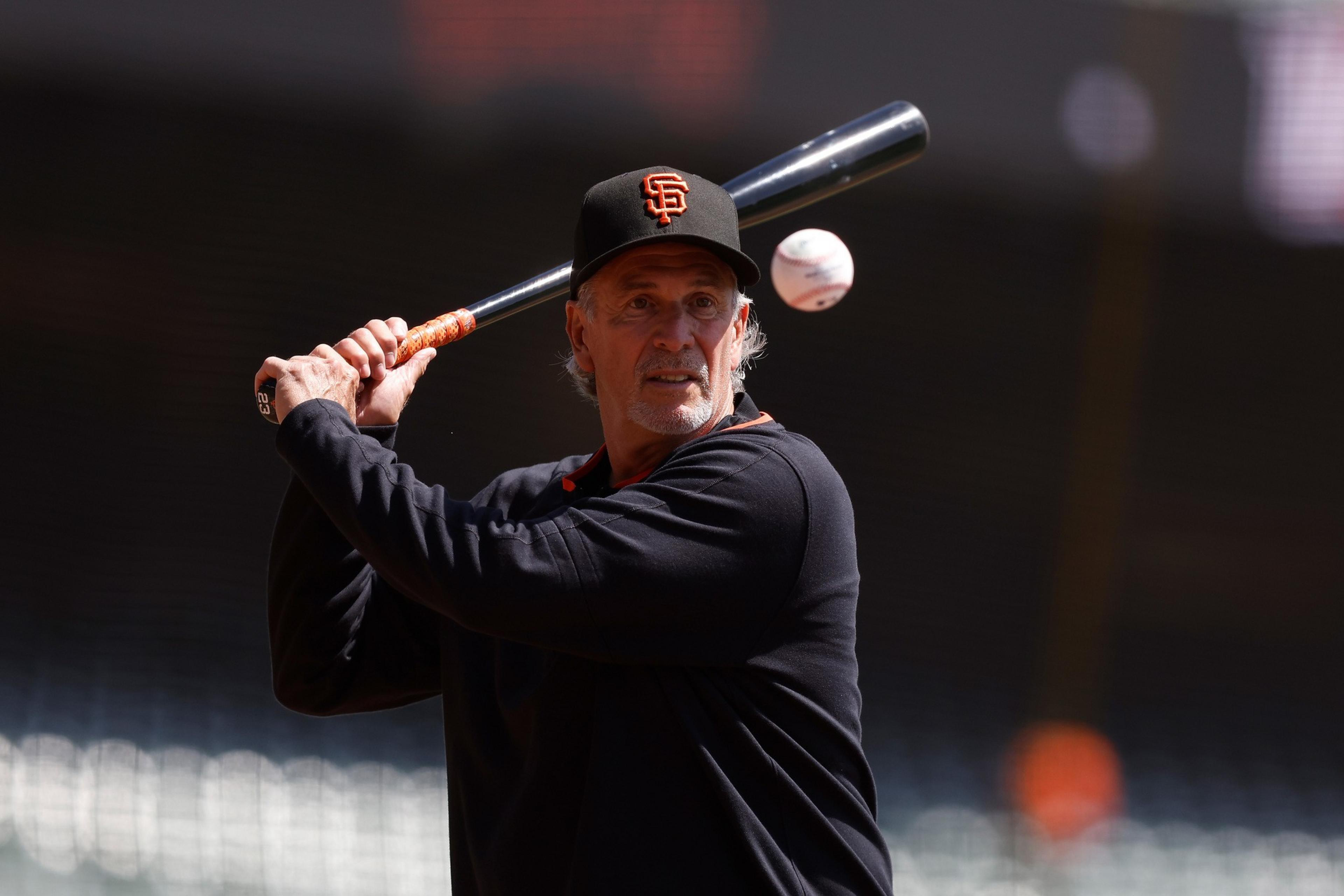 A man wearing a San Francisco Giants cap and black shirt is holding a baseball bat, preparing to hit a ball approaching him.