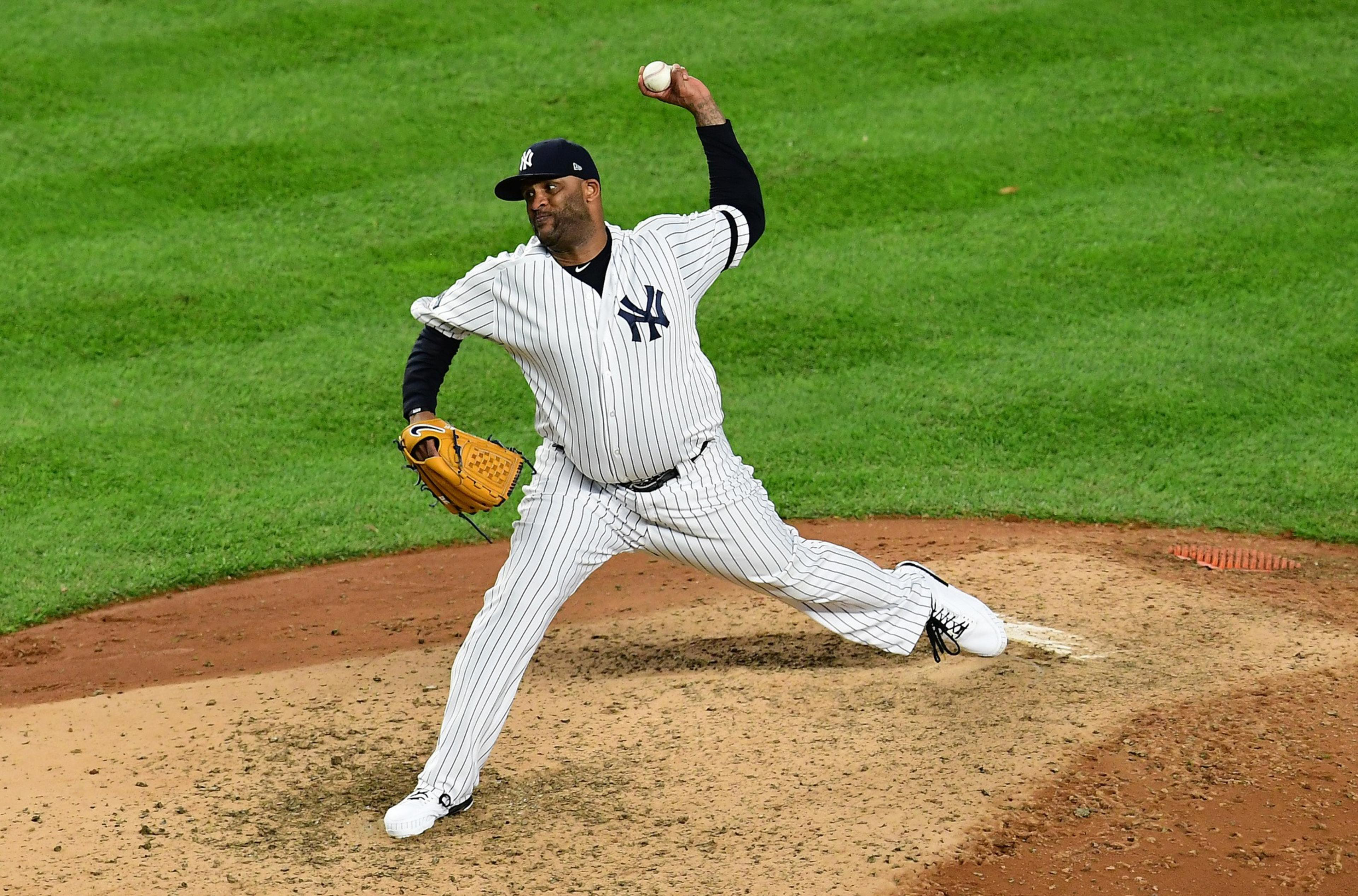 A baseball pitcher in a pinstriped uniform and cap is on the mound, mid-throw, with one foot up. The field is green, and he holds a glove in his left hand.