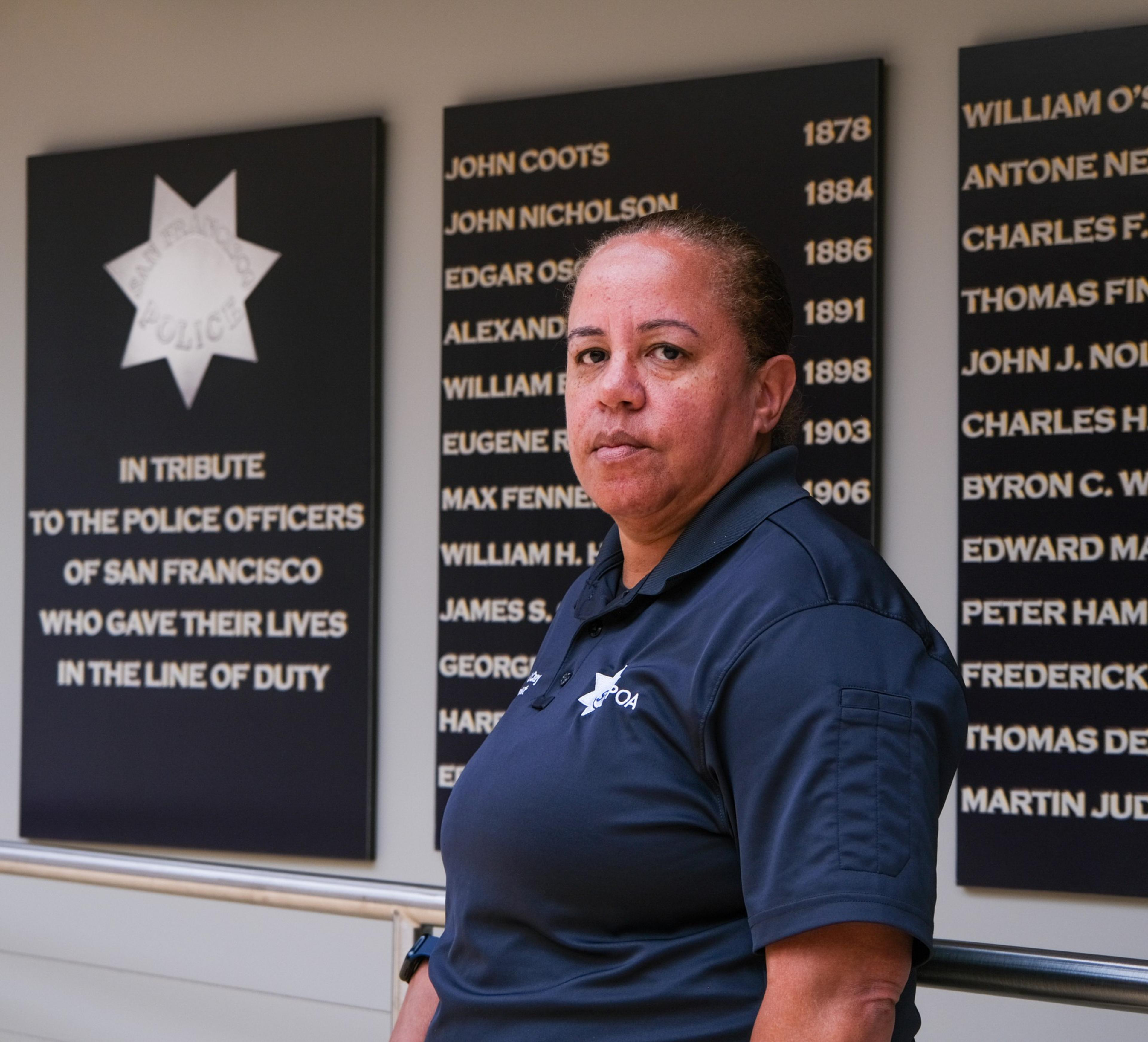 A person in a police uniform stands beside memorial plaques listing names of fallen San Francisco police officers, honoring those who died in the line of duty.