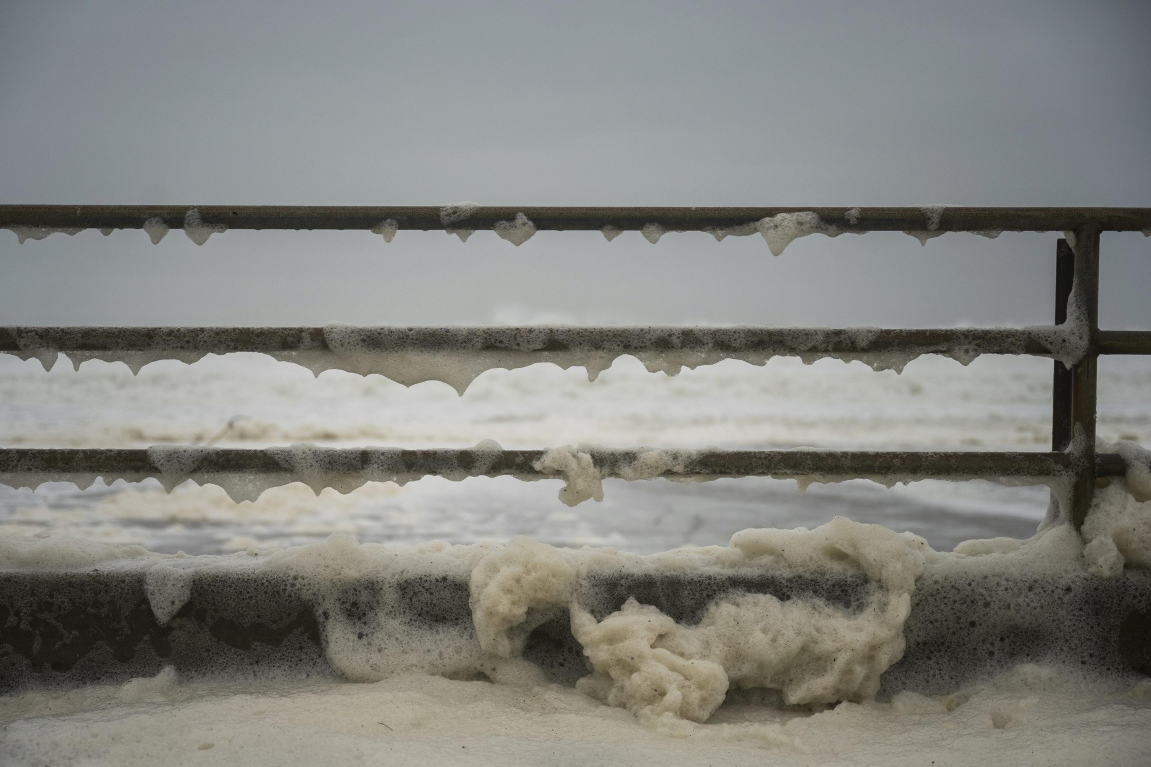 Waves smash up agains railing. 