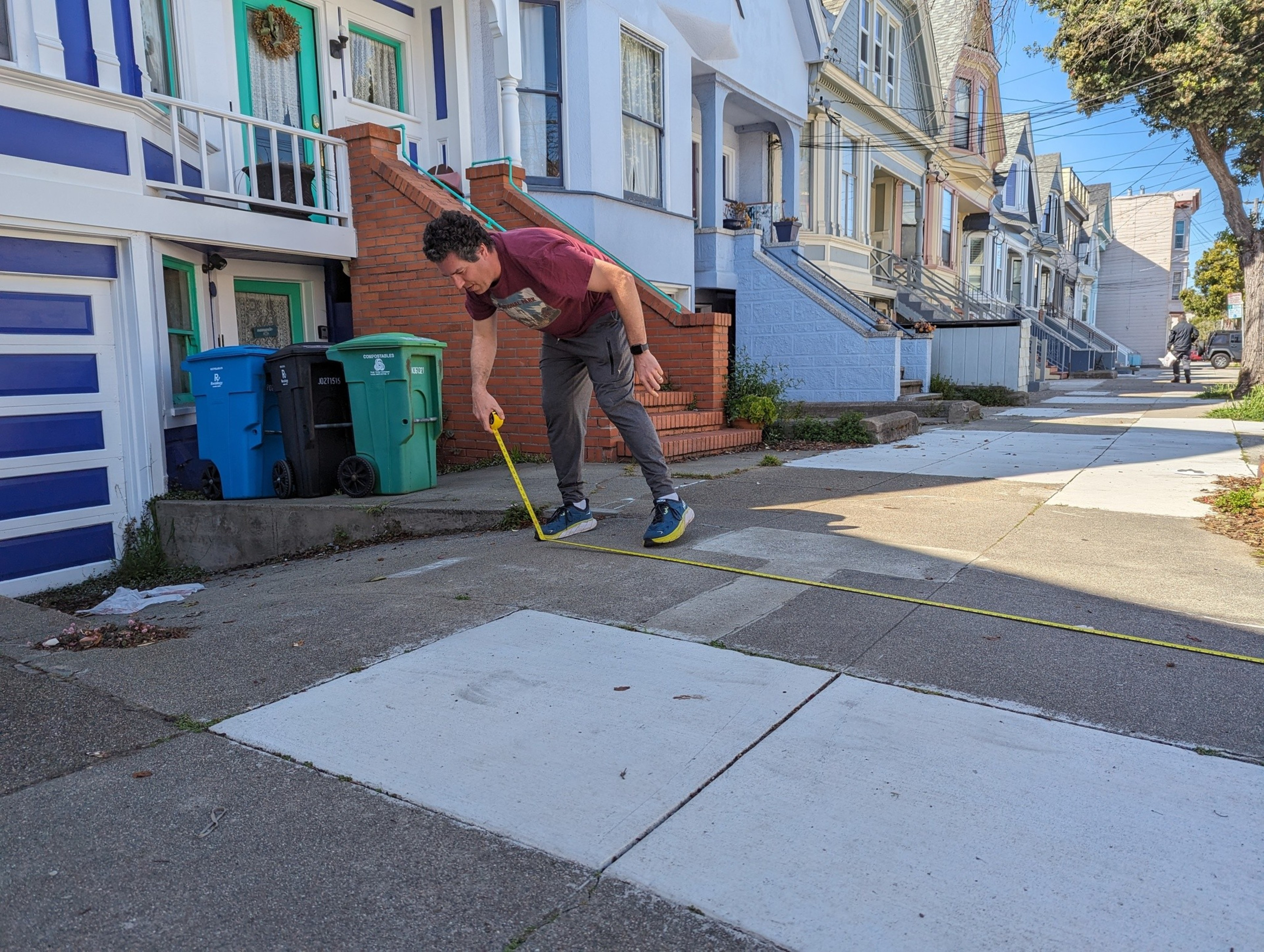 A man holds a measuring tape down to the sidewalk.