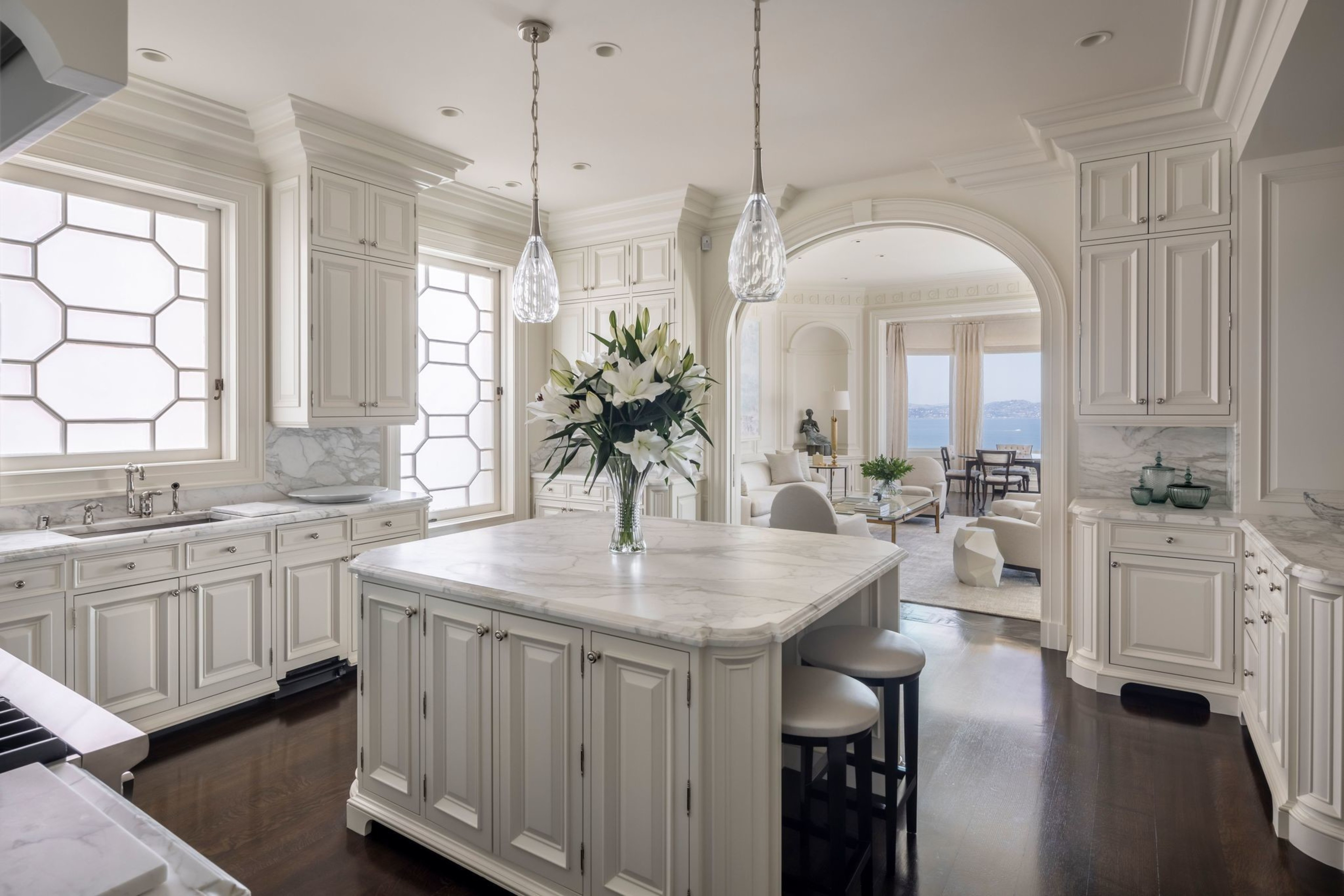 A kitchen with countertop, sink and island is visible next to an arched doorway leading to a living room.
