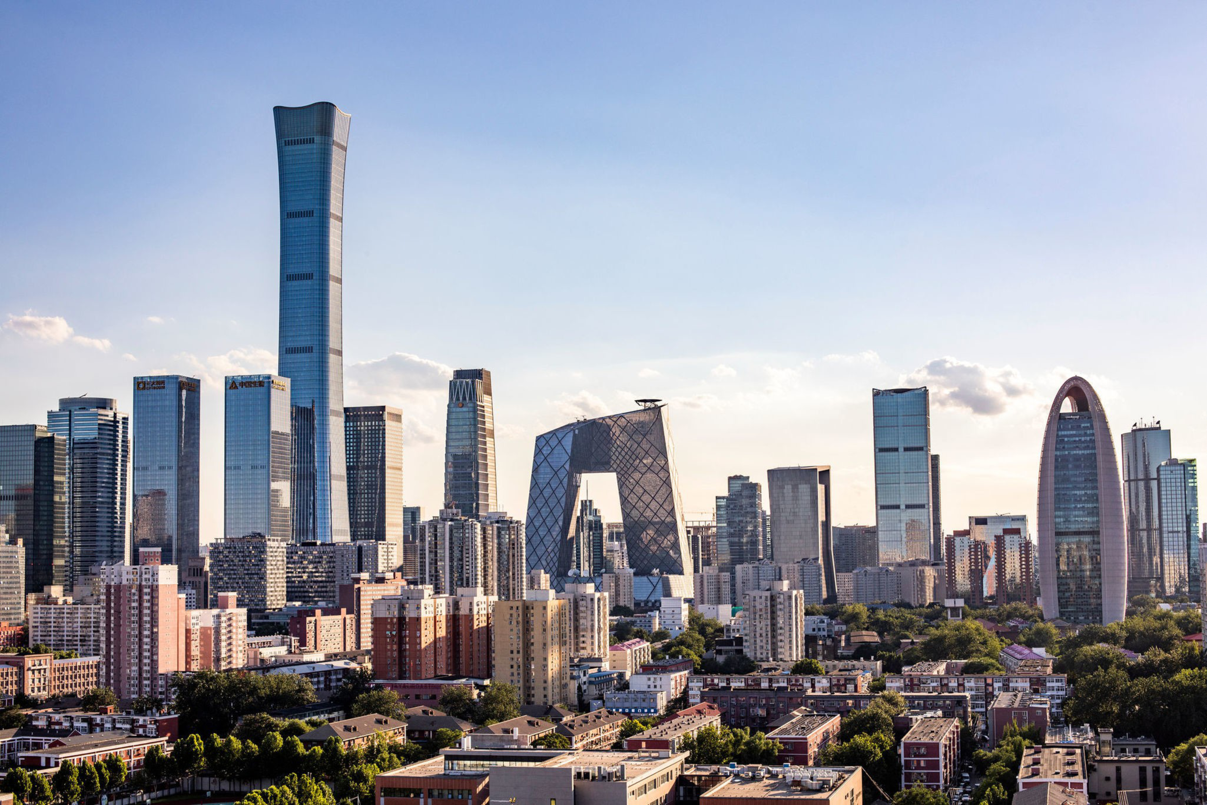 A modern city skyline with tall skyscrapers, including a twisted tower, a building with a large rectangular hole in the center, and a rounded oval-shaped tower.