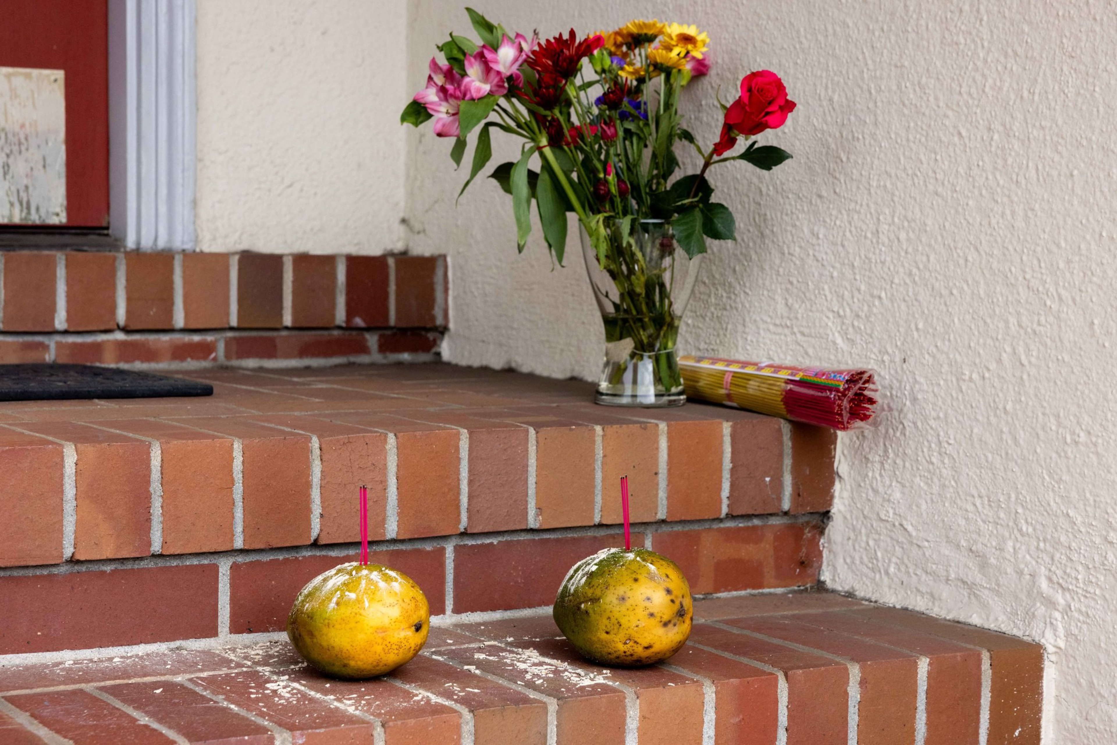 Two mangoes with incense sticks inserted are placed on brick steps, with a bouquet of colorful flowers and a bundle of incense sticks on the top step.