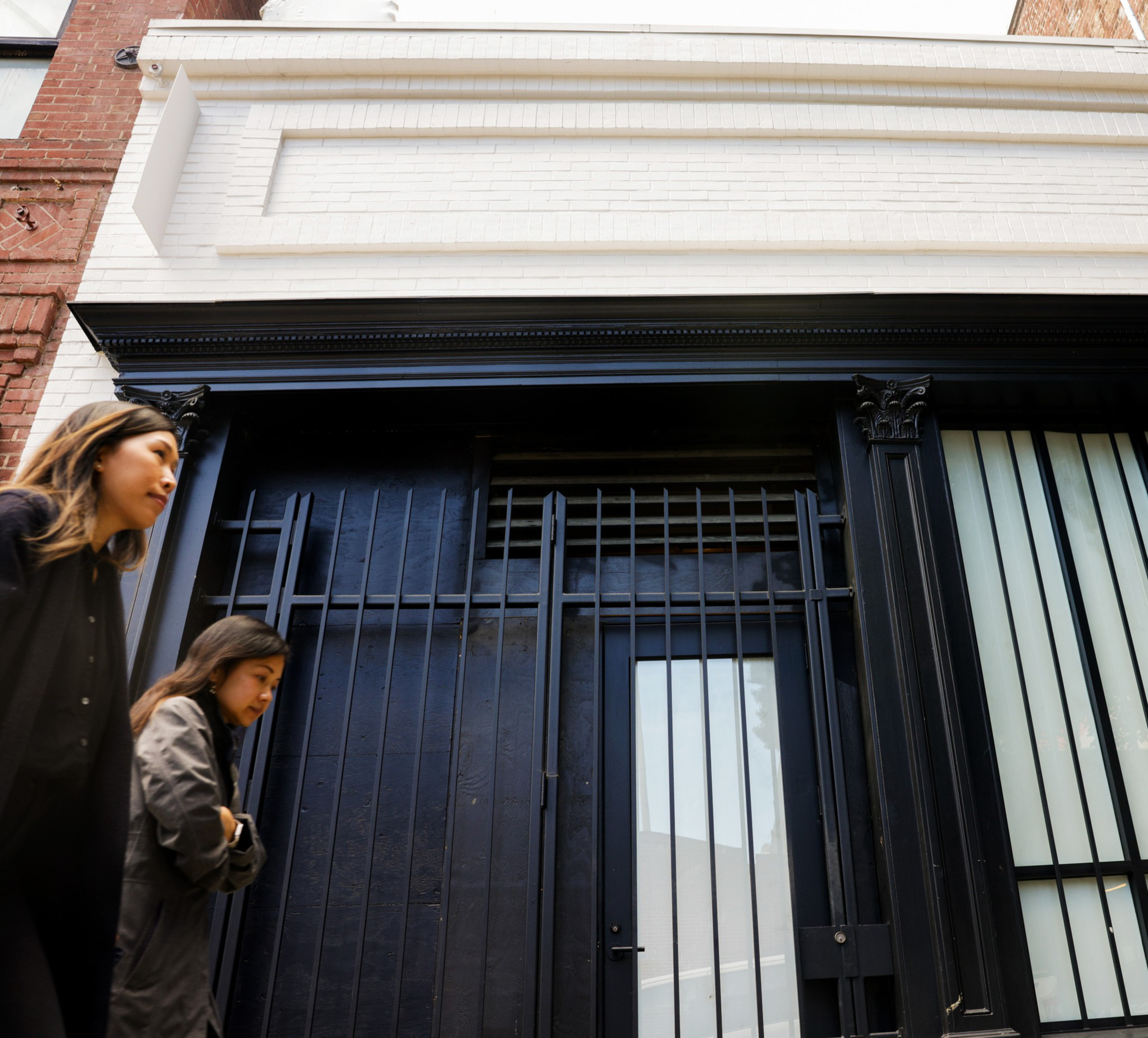 Two people walk past a dark building entrance with barred doors.