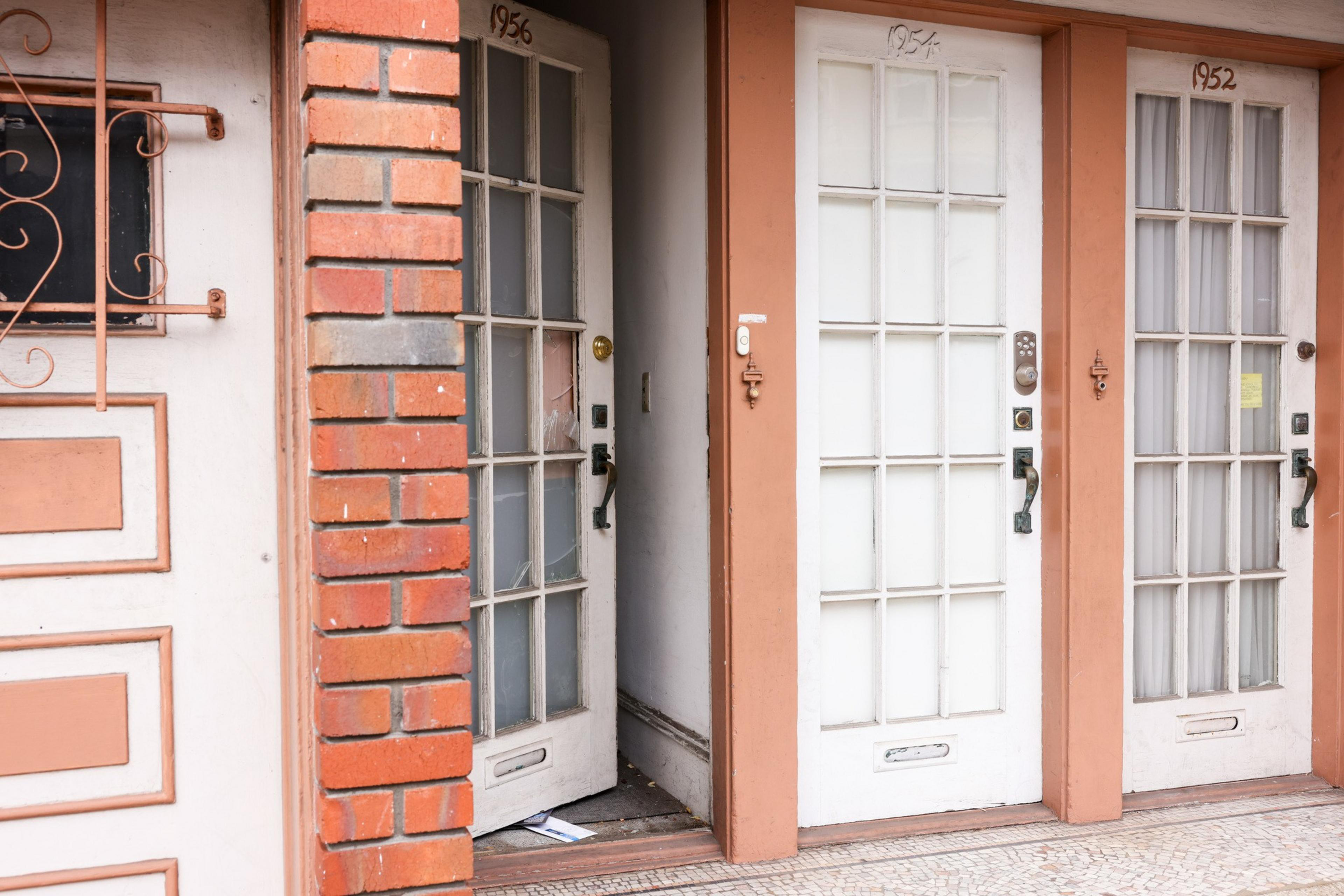 Three adjacent doors with glass panels have the numbers 1956, 1954, and 1952 above them. One door is slightly open, revealing a dark interior.