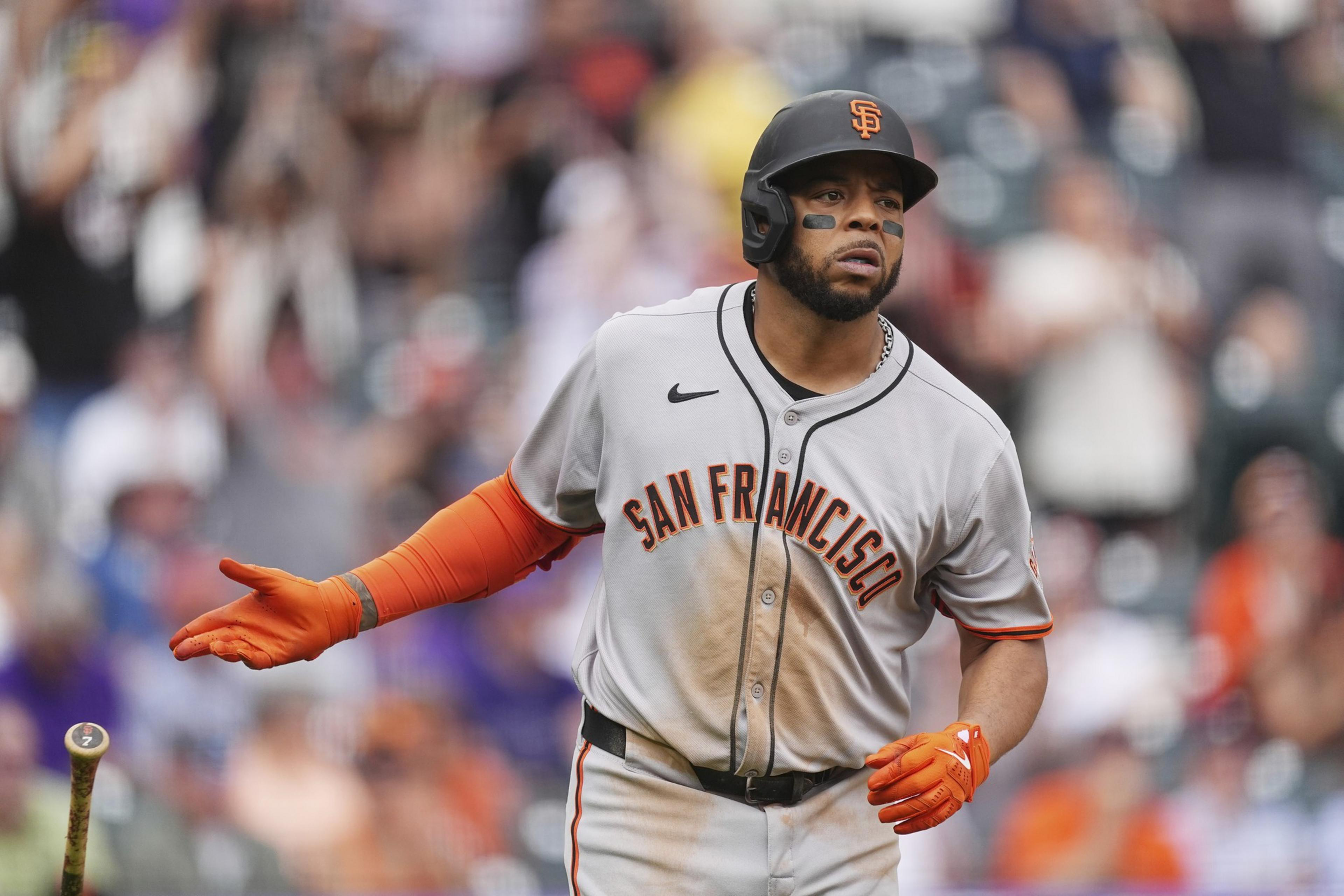 A baseball player in a San Francisco Giants uniform swings a bat. He wears orange batting gloves and a helmet, with eye black applied to his face.