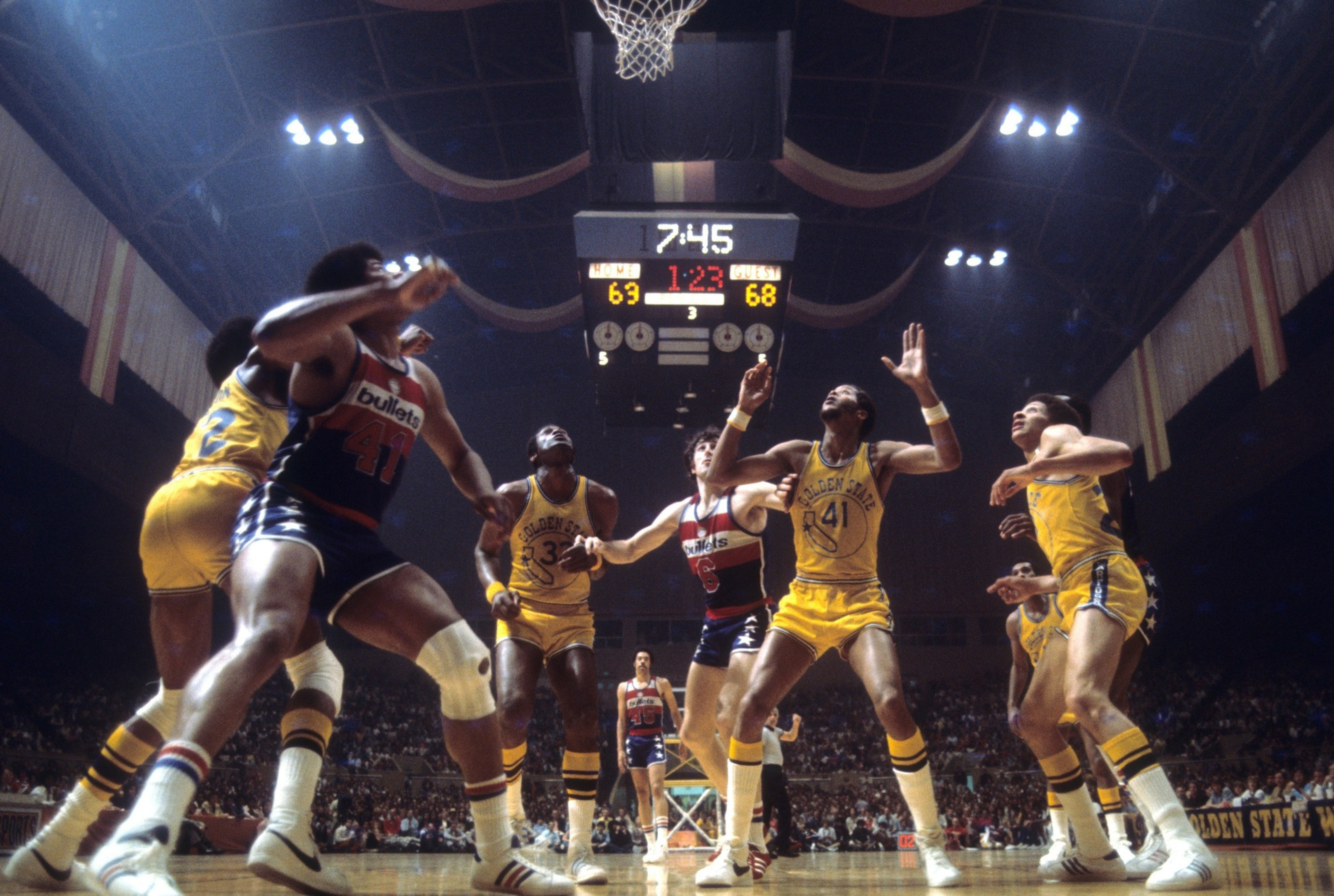 A basketball game in action, with players vying for the ball under the hoop.