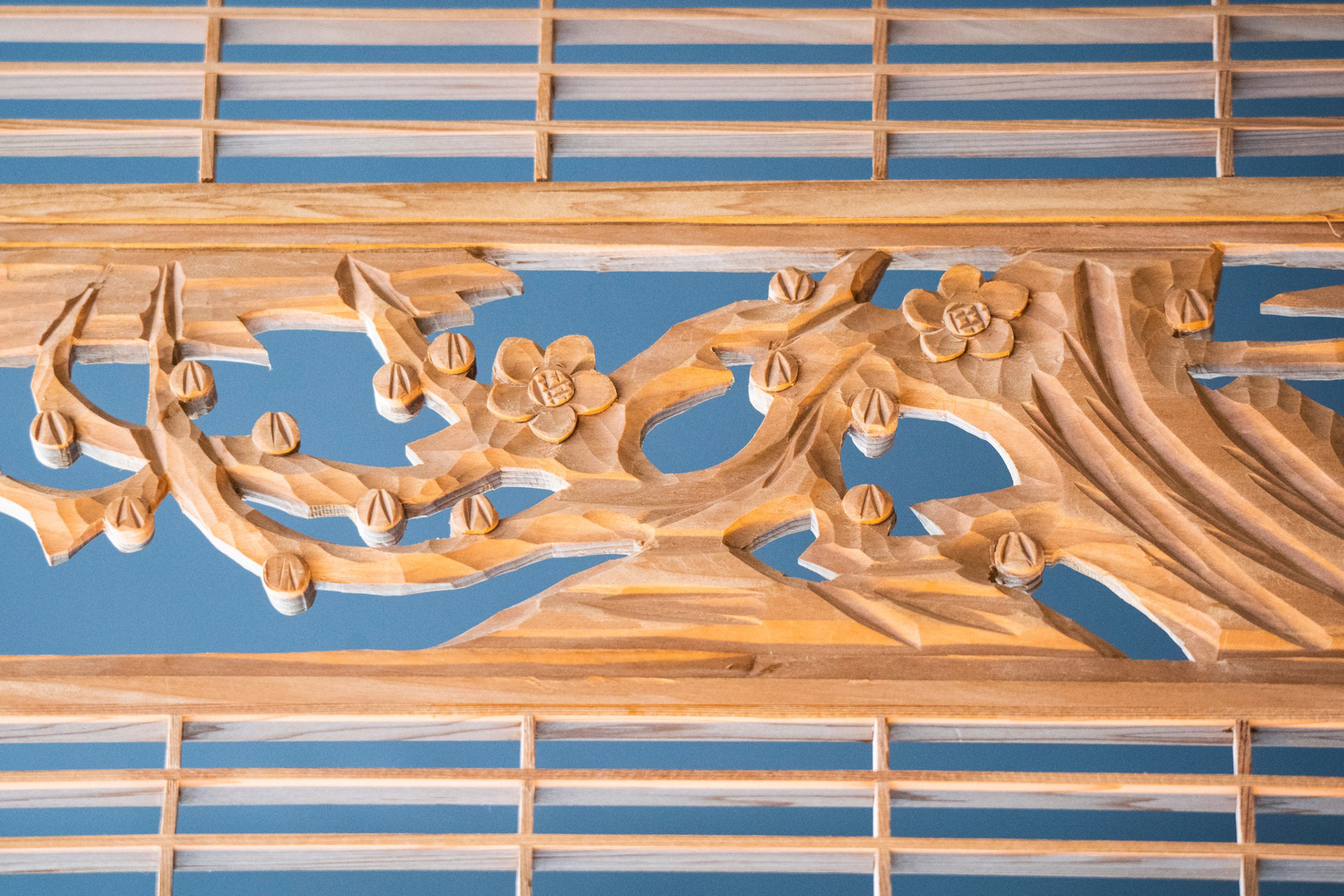 The image shows an intricately carved wooden panel featuring a floral design with flowers and branches set against a blue background.